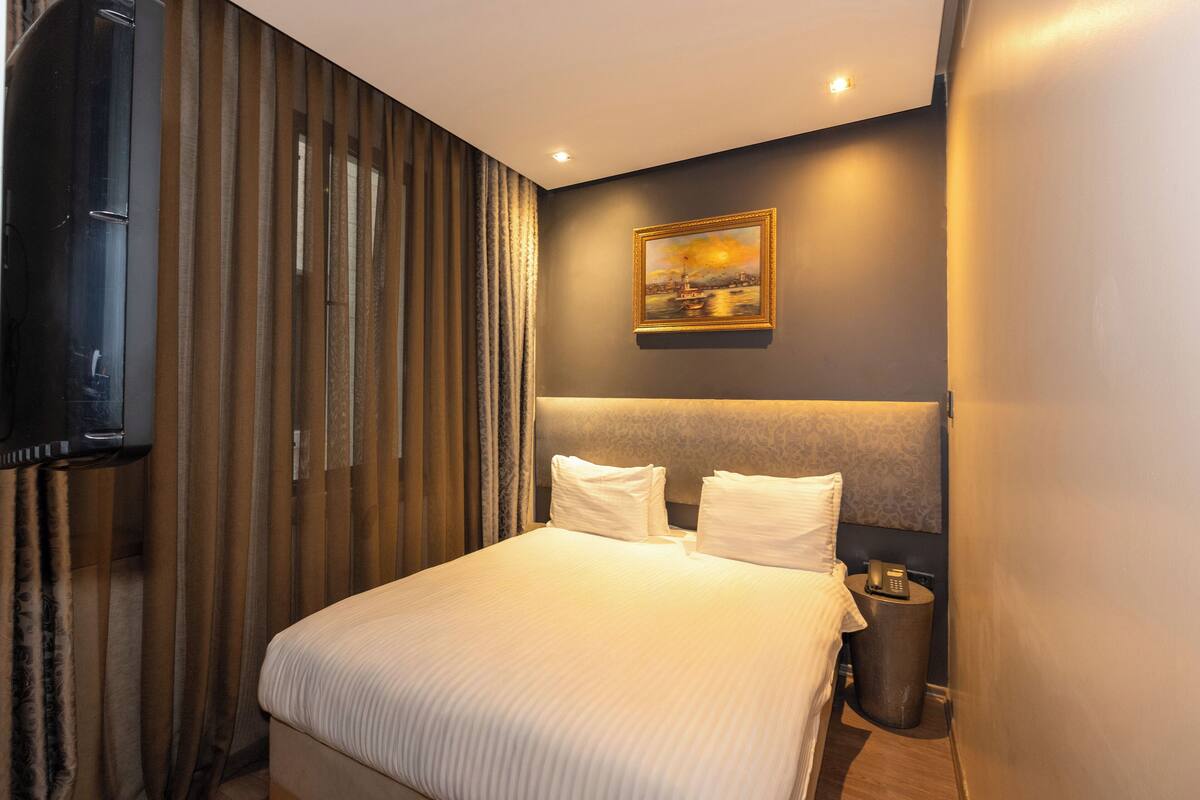 Une chambre d’hôtel avec un grand lit, un téléviseur fixé au mur, un tableau accroché au mur et un téléphone sur la table de chevet.