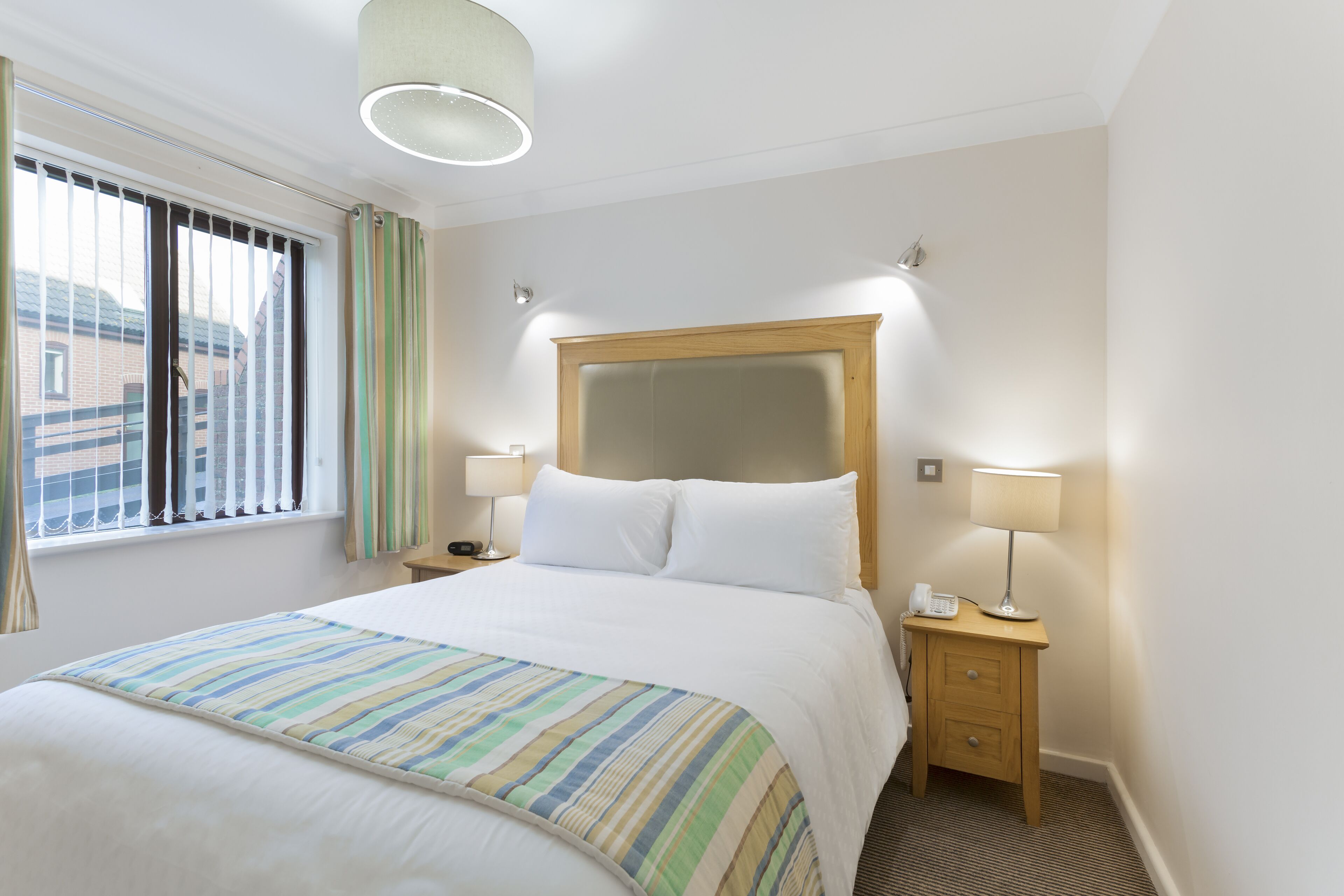 Une chambre d’hôtel avec un grand lit, deux tables de chevet avec des lampes, une fenêtre avec des rideaux et une vue sur les bâtiments environnants.
