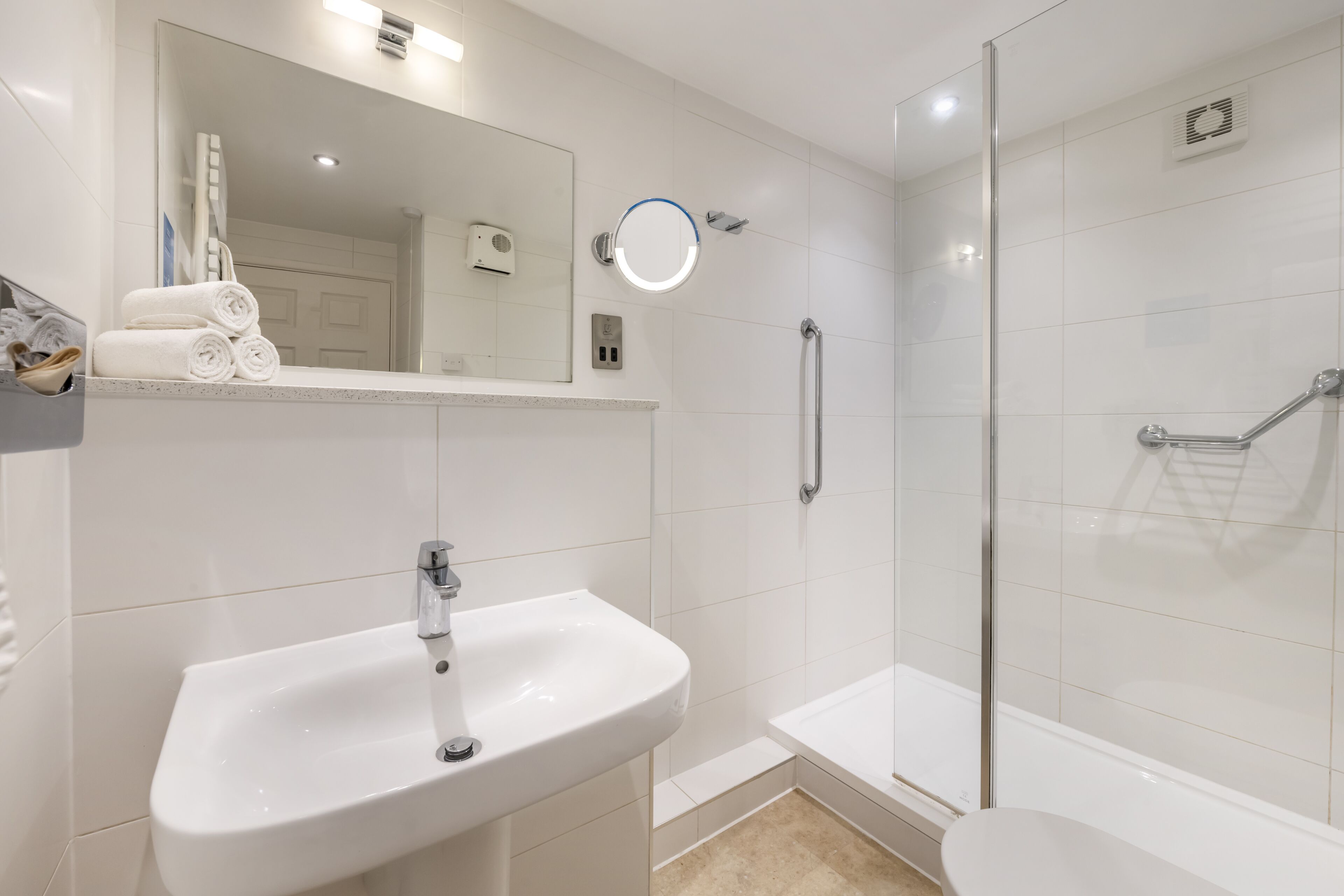 A modern bathroom with a white sink, a glass-enclosed shower, and a mirror above the sink.