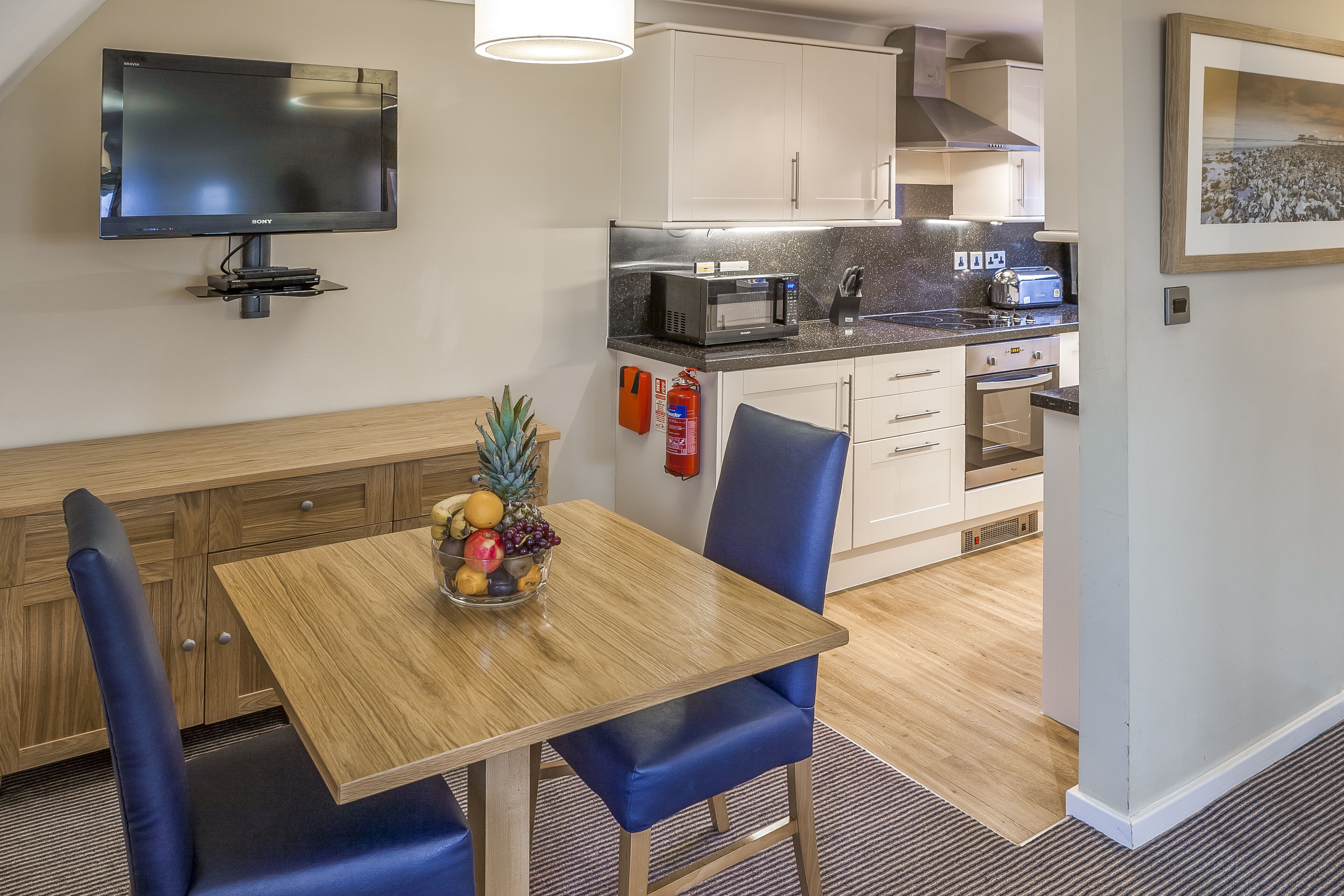 A compact kitchen with a microwave, toaster, and a small dining area with a fruit bowl.