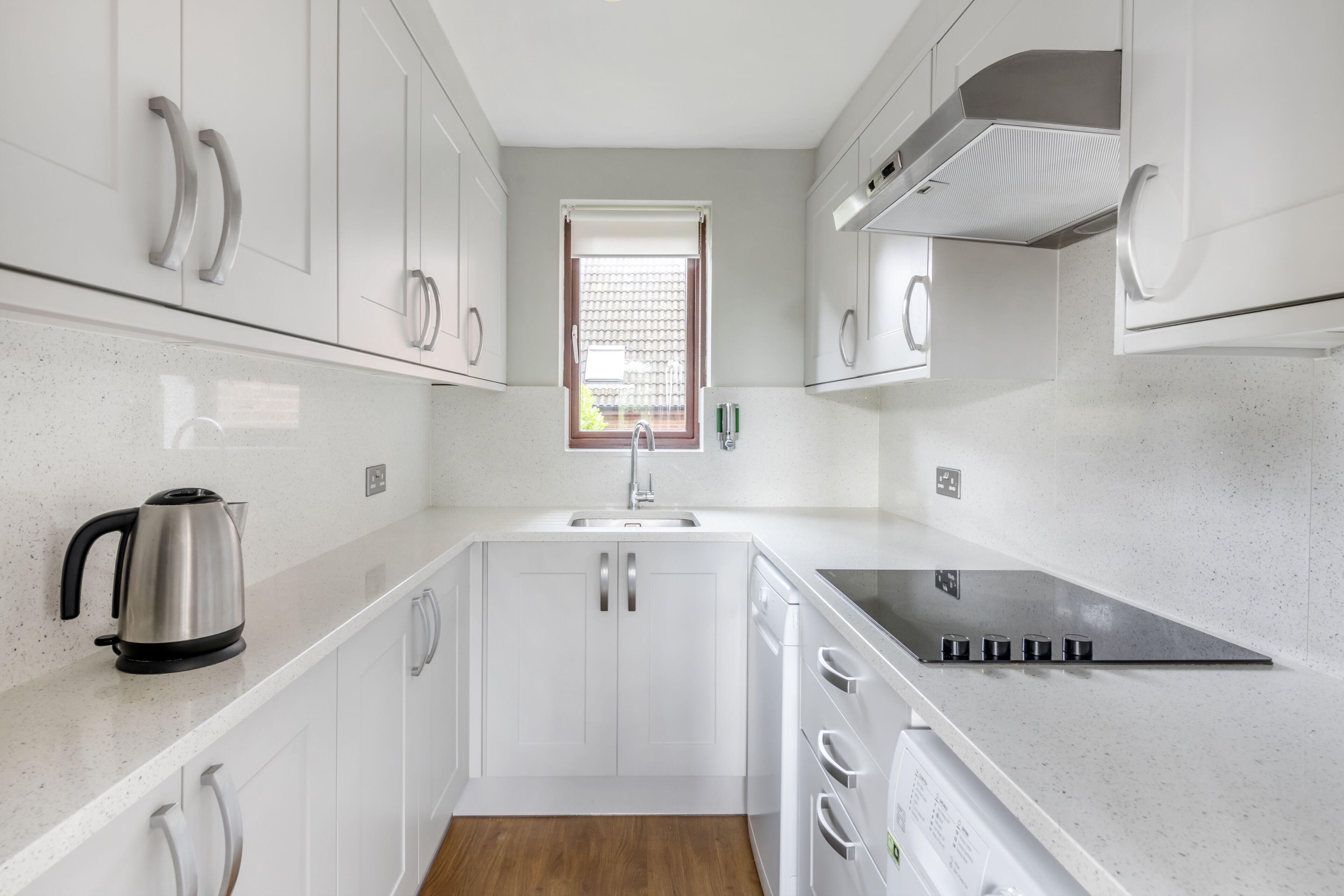 Une cuisine moderne avec des meubles blancs, une bouilloire en acier inoxydable, un évier et une cuisinière.