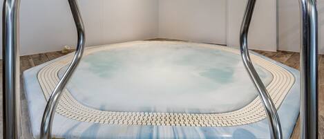 A hot tub with metal handrails, surrounded by a white textured floor, in a room with white walls and a wooden floor.