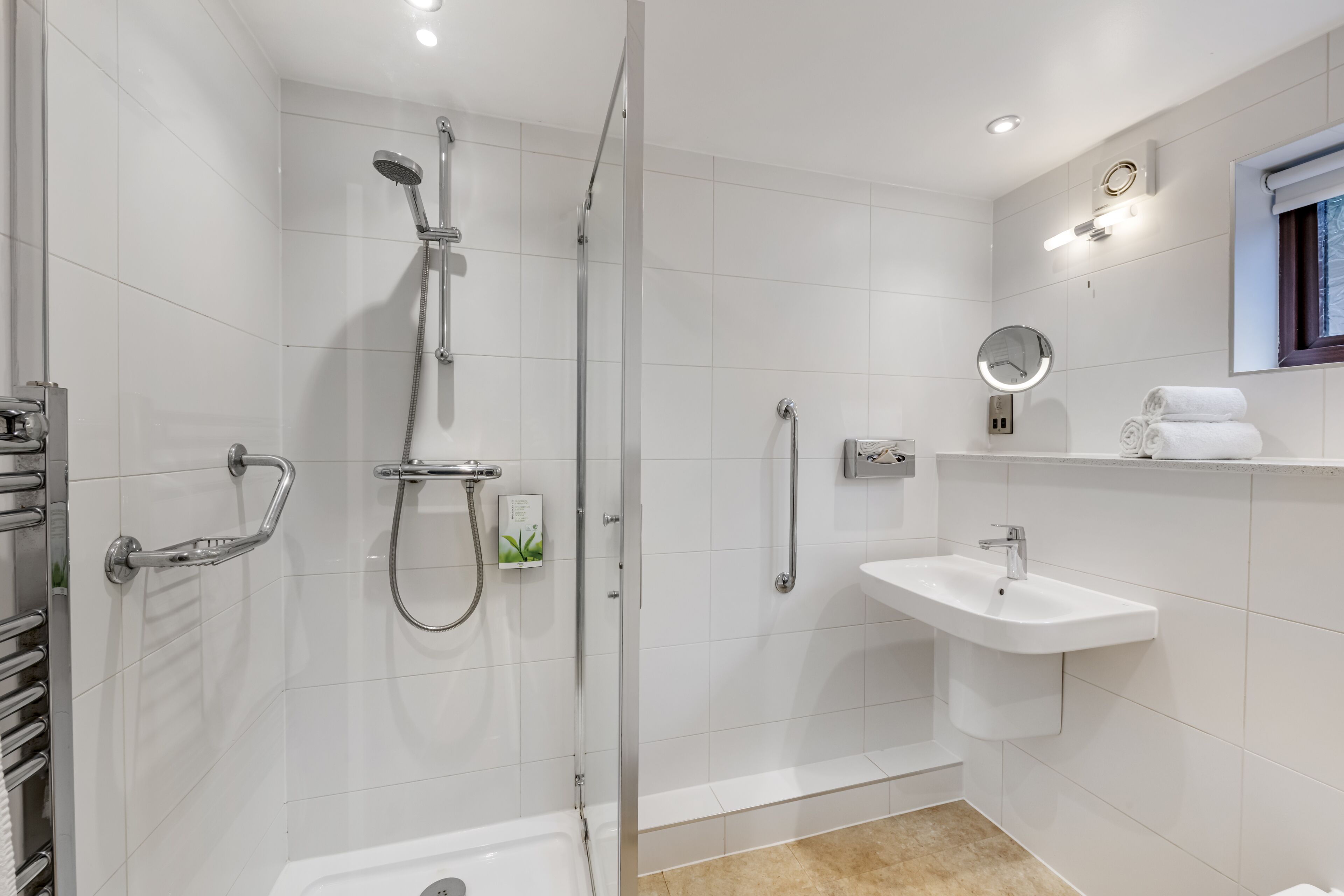 Un baño moderno con ducha de vidrio, lavamanos blanco y un espejo pequeño.