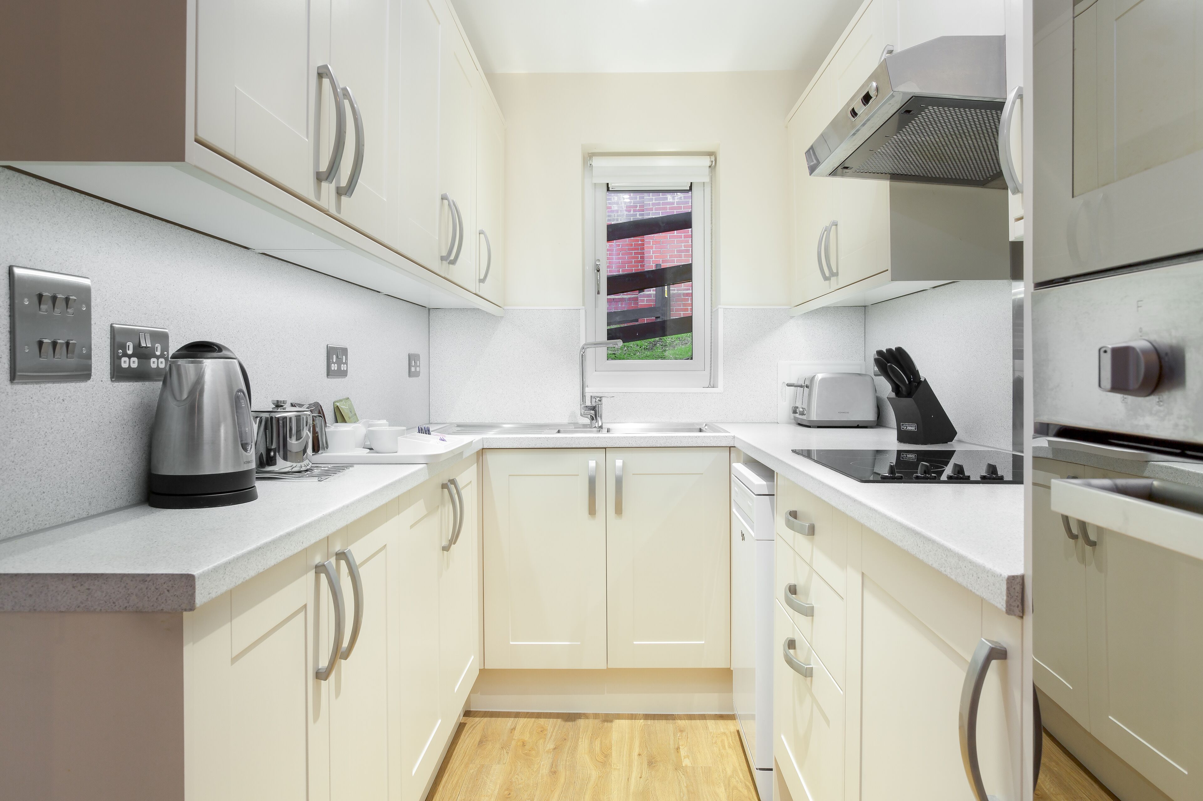 A modern kitchen with white cabinetry, stainless steel appliances, and a window with a view of a brick wall.