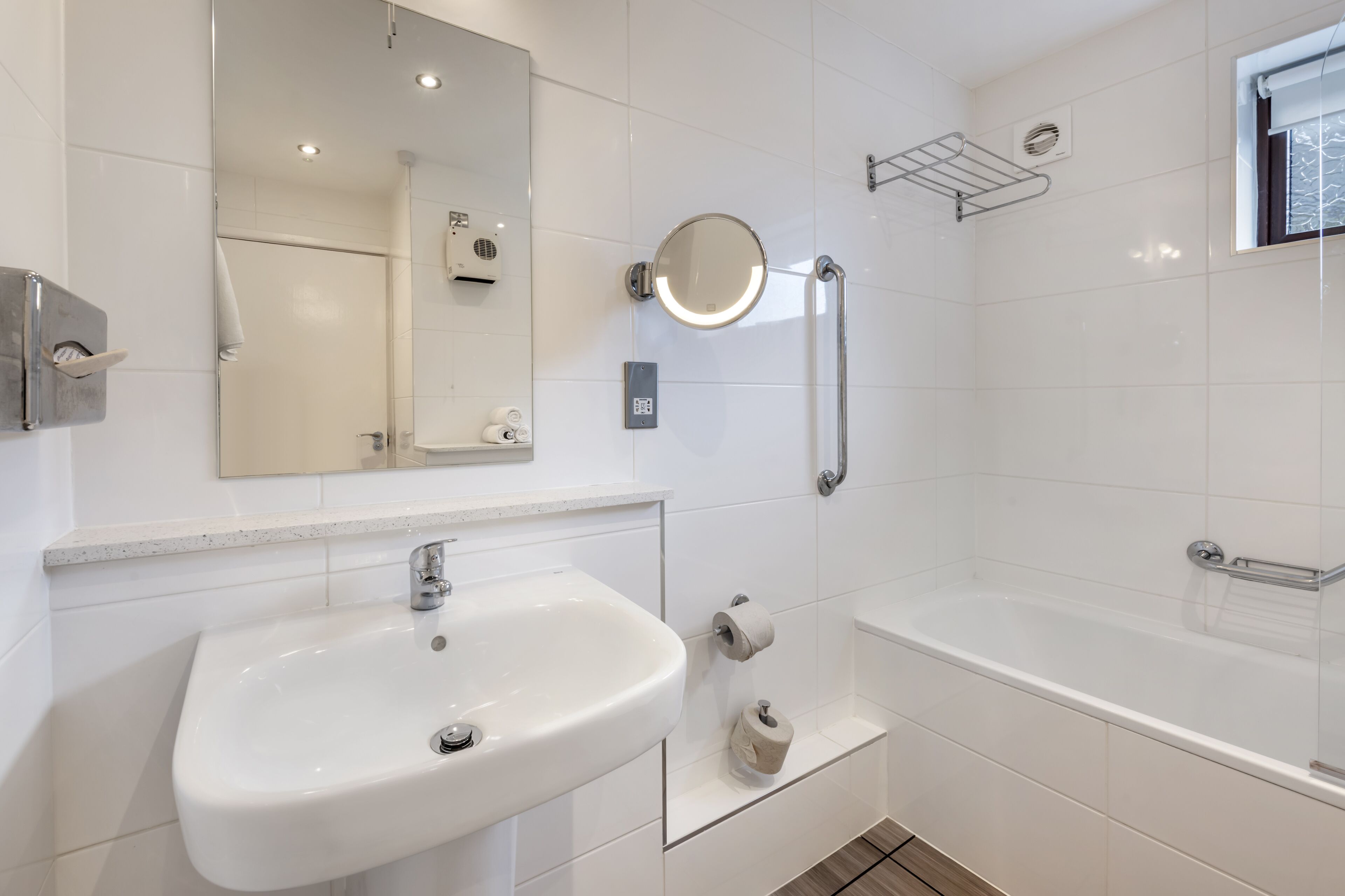 A modern bathroom with a white sink, a mirror, a handheld showerhead, and a bathtub.