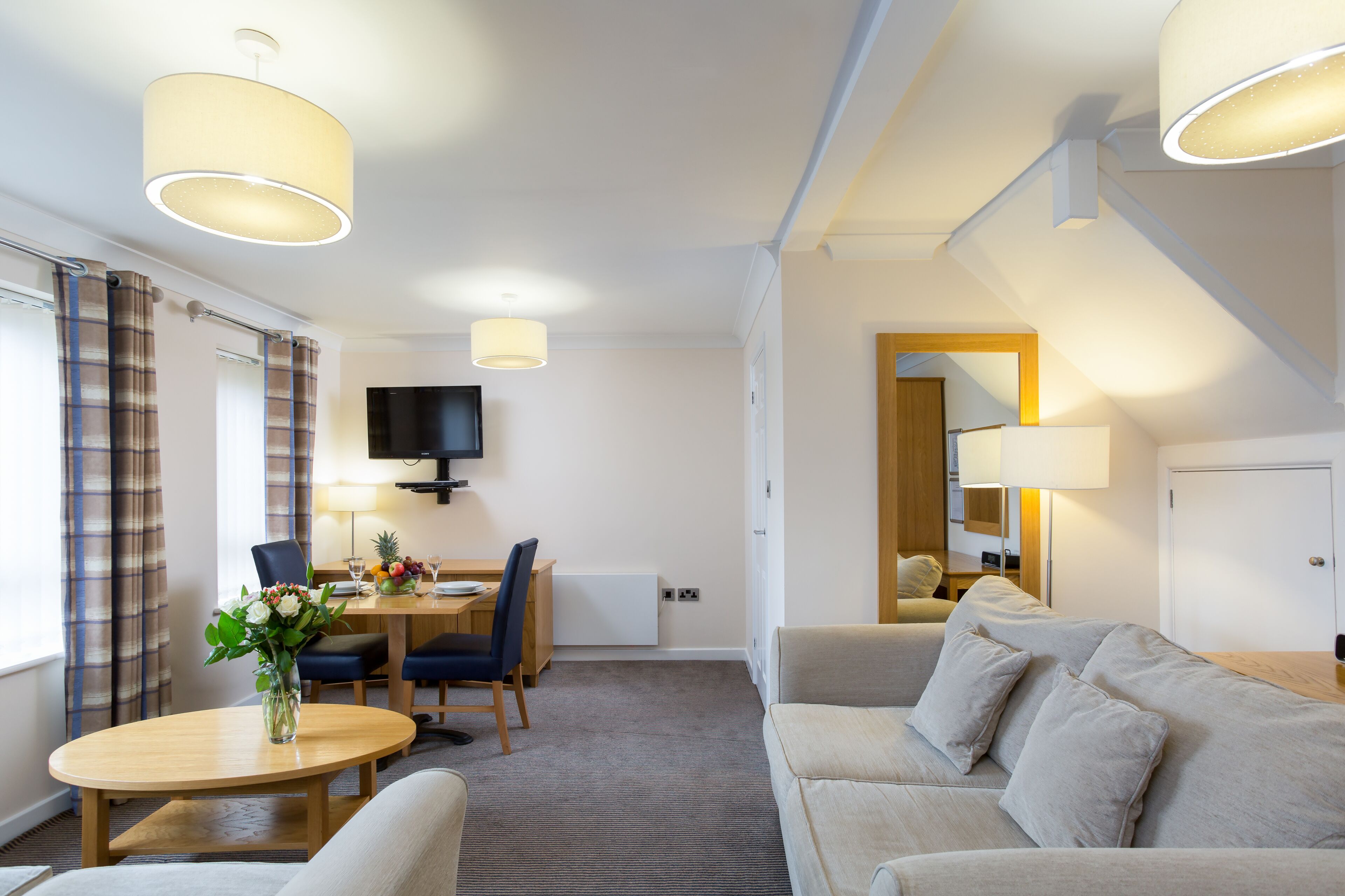 Habitación de hotel con comedor, sofá, televisión y lámpara.