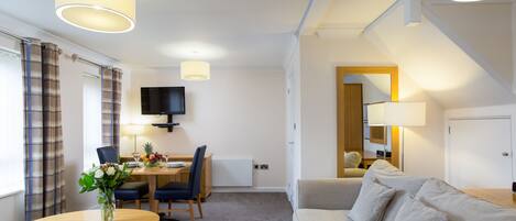 Habitación de hotel con comedor, sofá, televisión y lámpara.