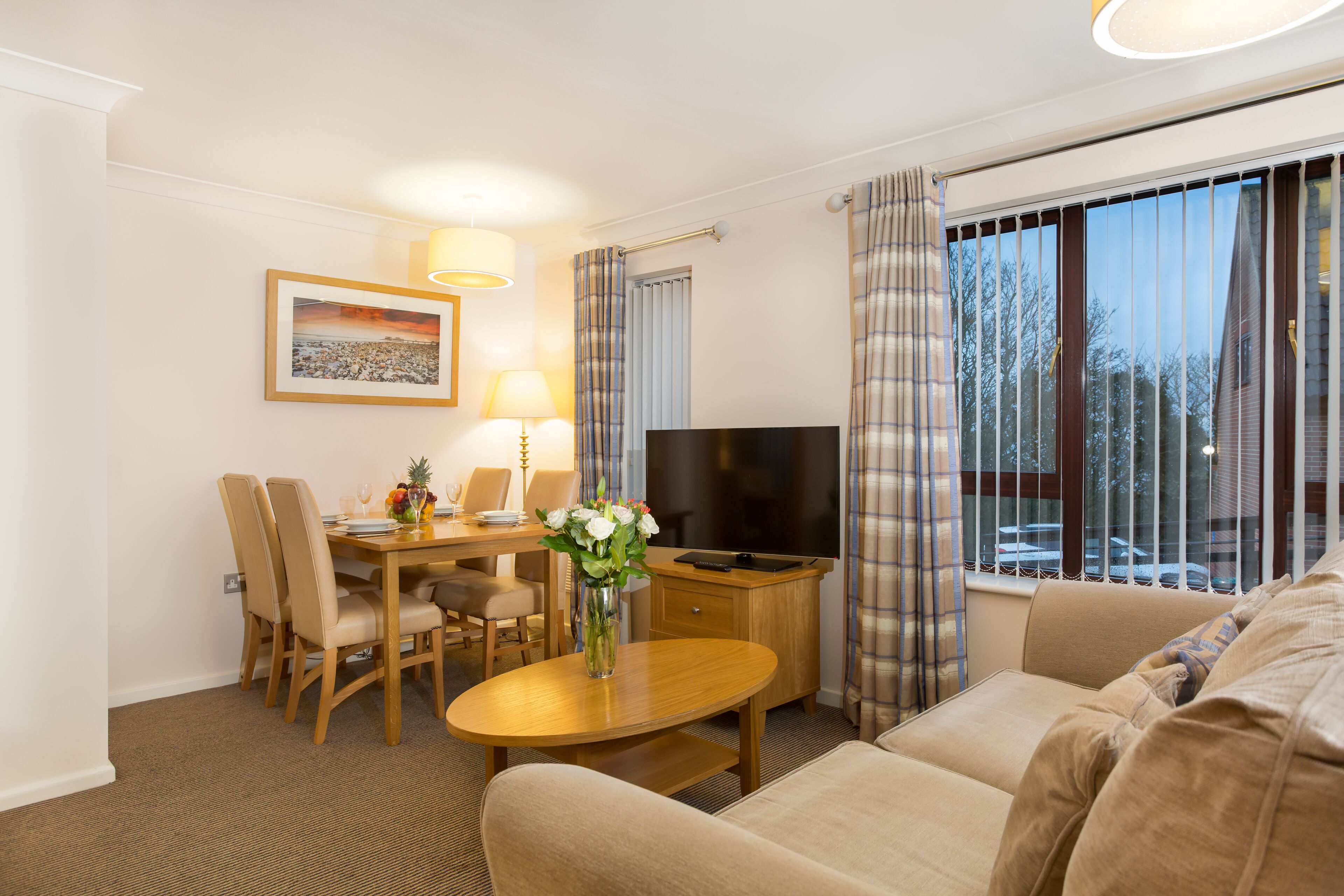 Een hotelkamer met een eethoek, een televisie, een bank en een raam met gordijnen.