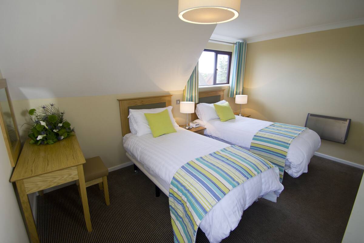 A hotel room with two beds, a desk, a lamp, and a window with curtains.