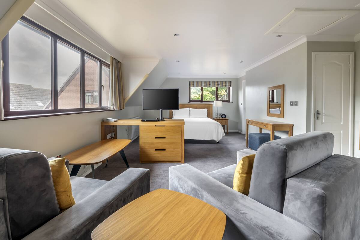 A modern bedroom with a large window, a desk, a bed, and a seating area.