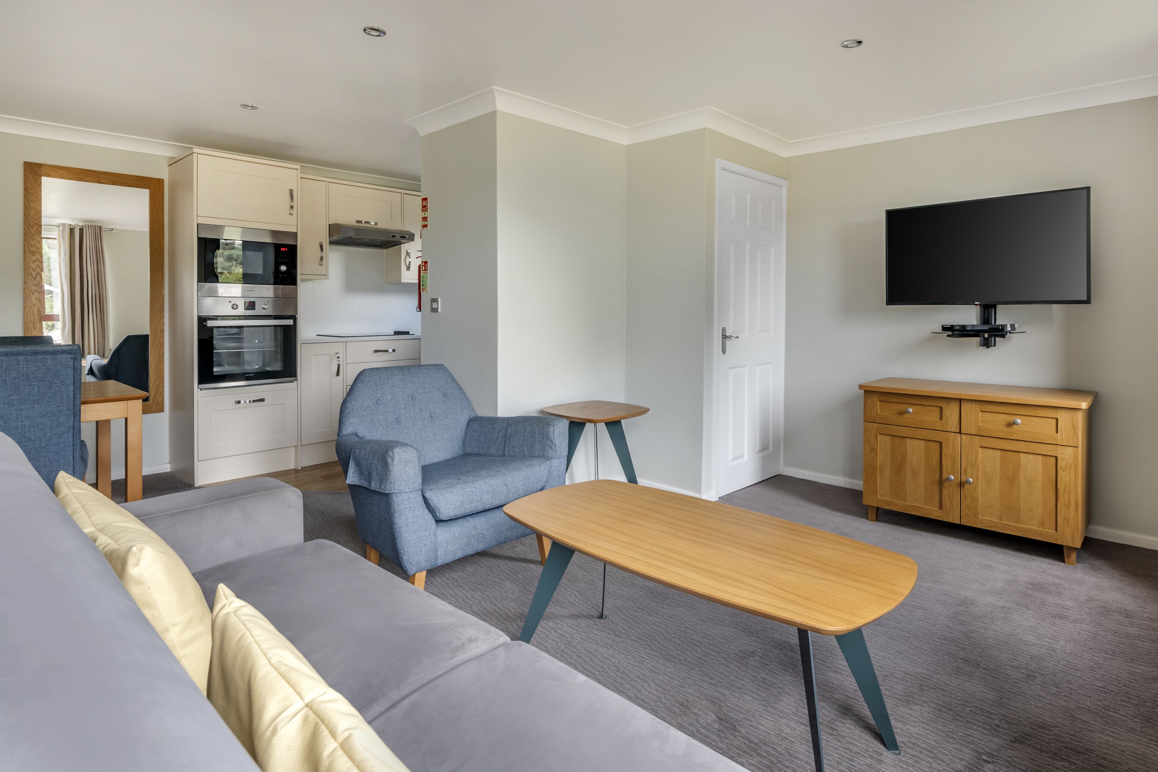 A modern living room with a sofa, a coffee table, a television, and a kitchen area with appliances.