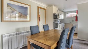 A dining area with a wooden table and blue chairs, a kitchen with modern appliances, and a framed picture on the wall.
