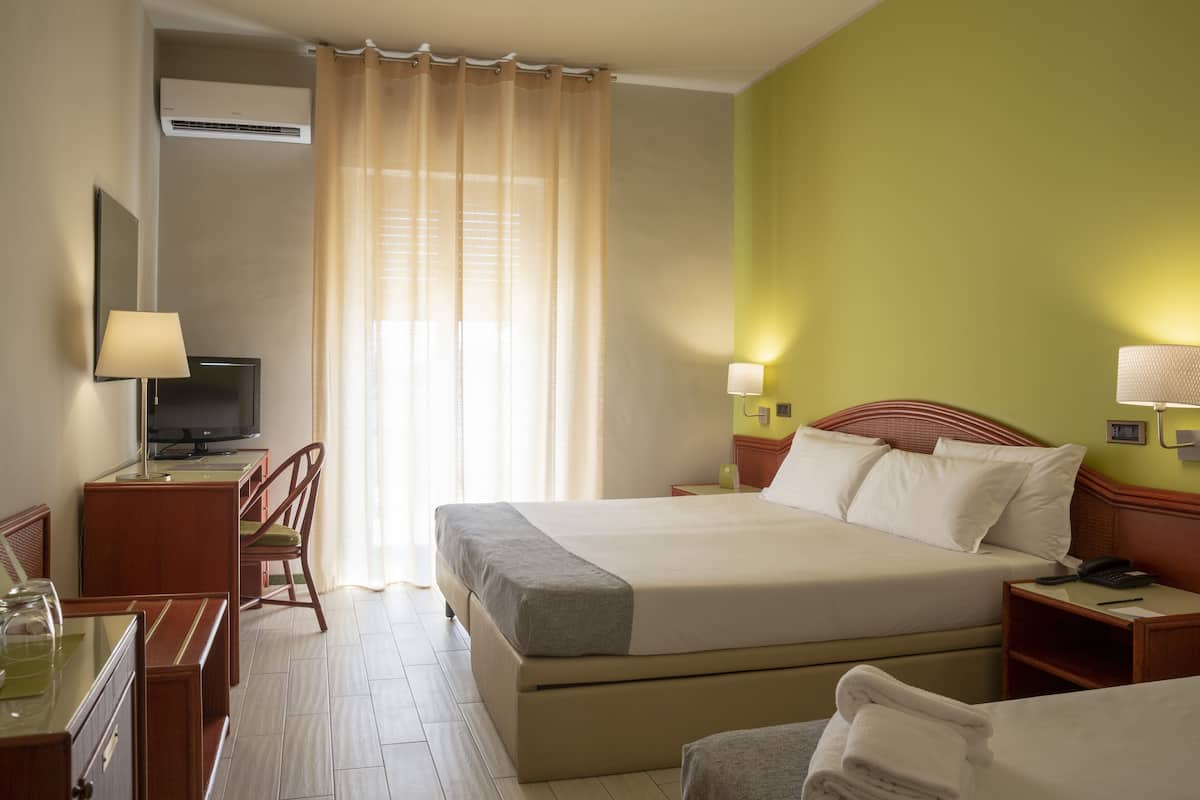 A hotel room with a bed, bedside tables, a desk with a chair, a television, and a window with curtains.