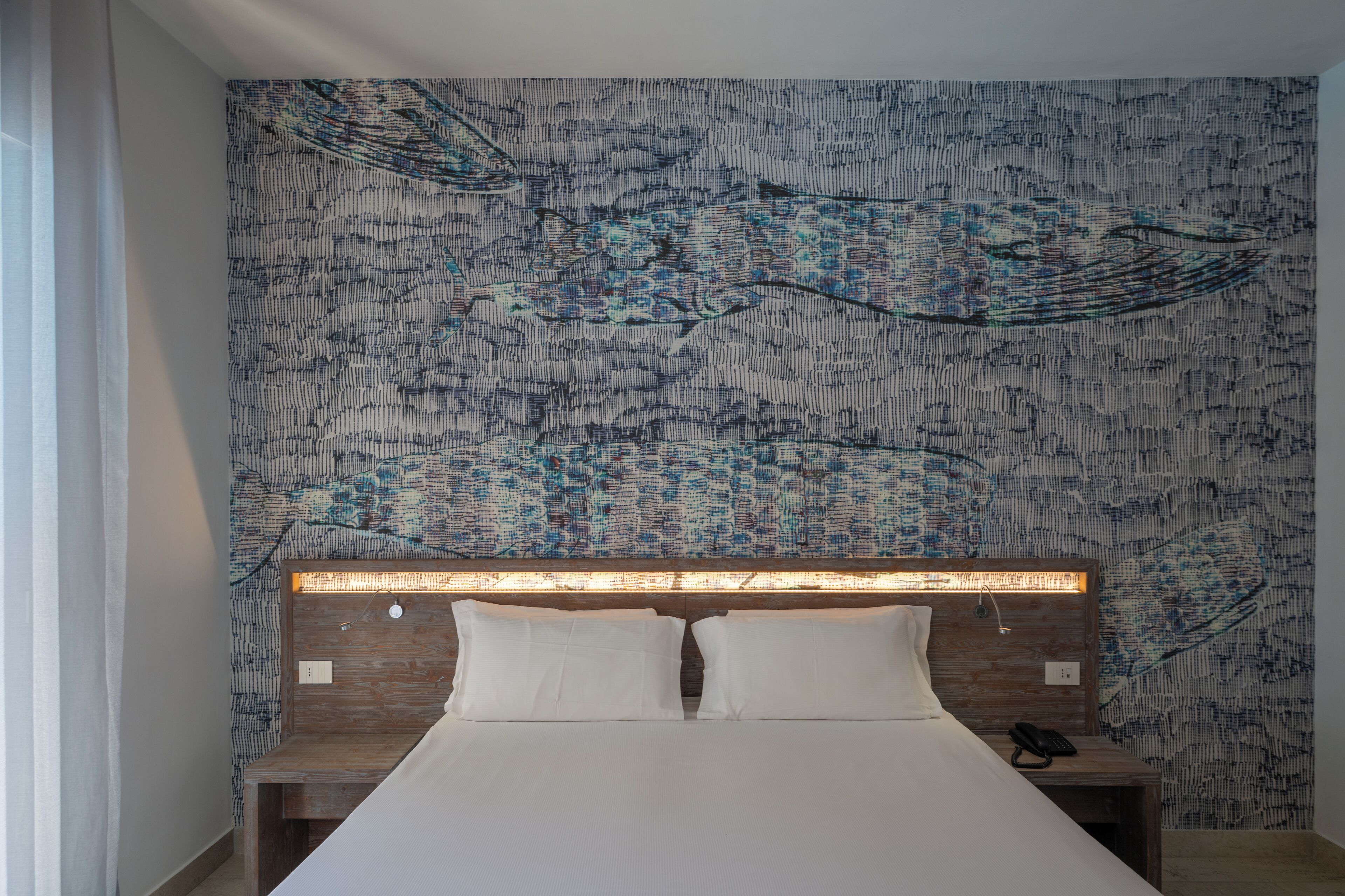 A bedroom with a patterned wall, a wooden headboard, and a bedside table with a phone.