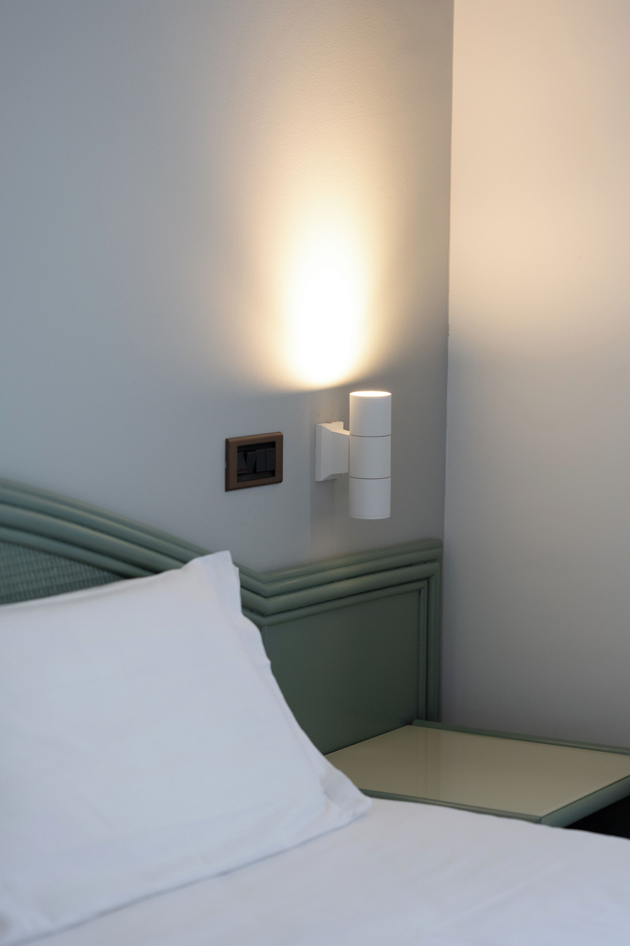 Une chambre d’hôtel avec un lit, une table de chevet et un luminaire fixé au mur.