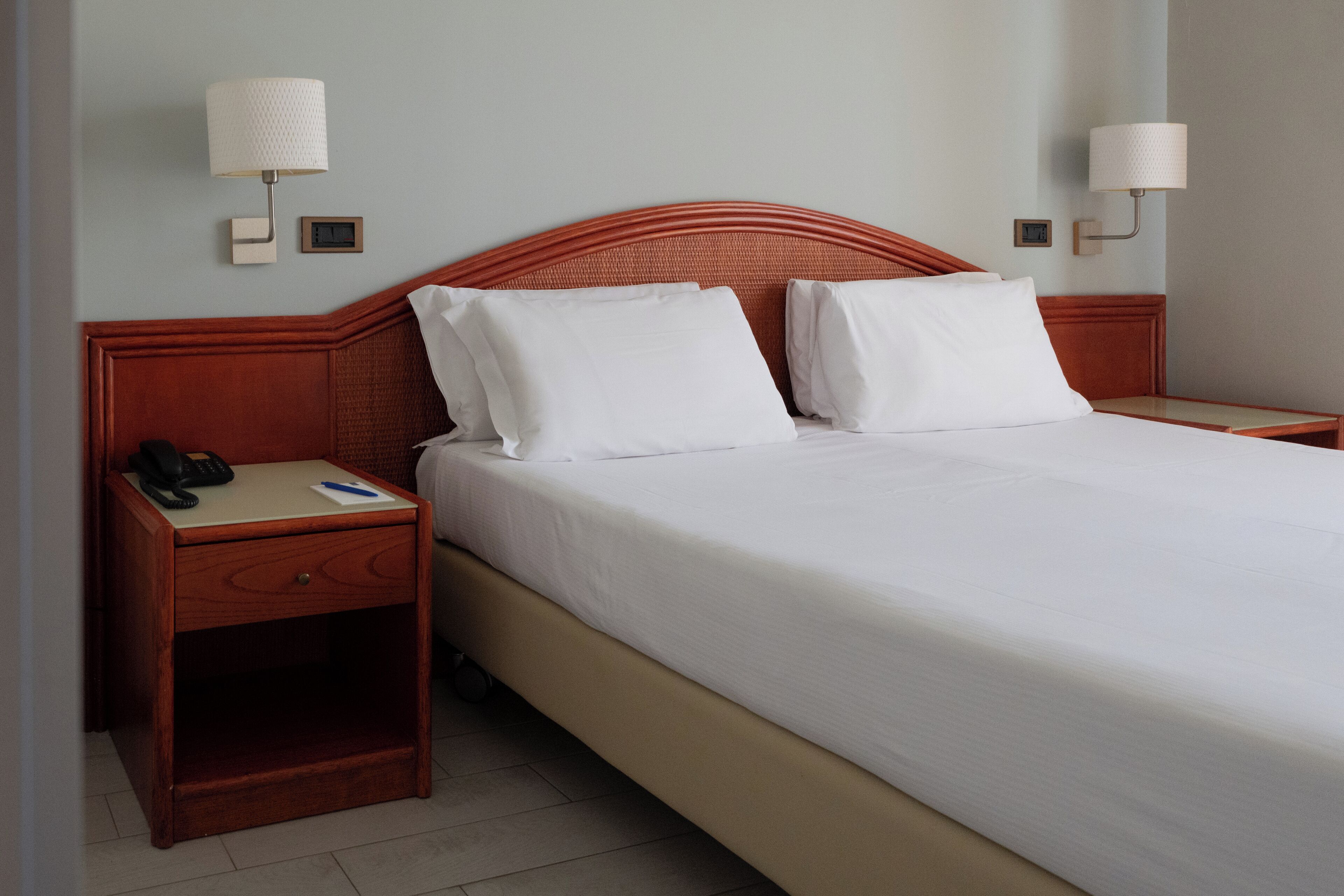 A hotel room with a single bed, a nightstand with a phone, and two wall-mounted lamps.