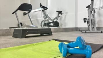 Un gimnasio con equipo de ejercicio, un espejo y una colchoneta verde en el suelo.