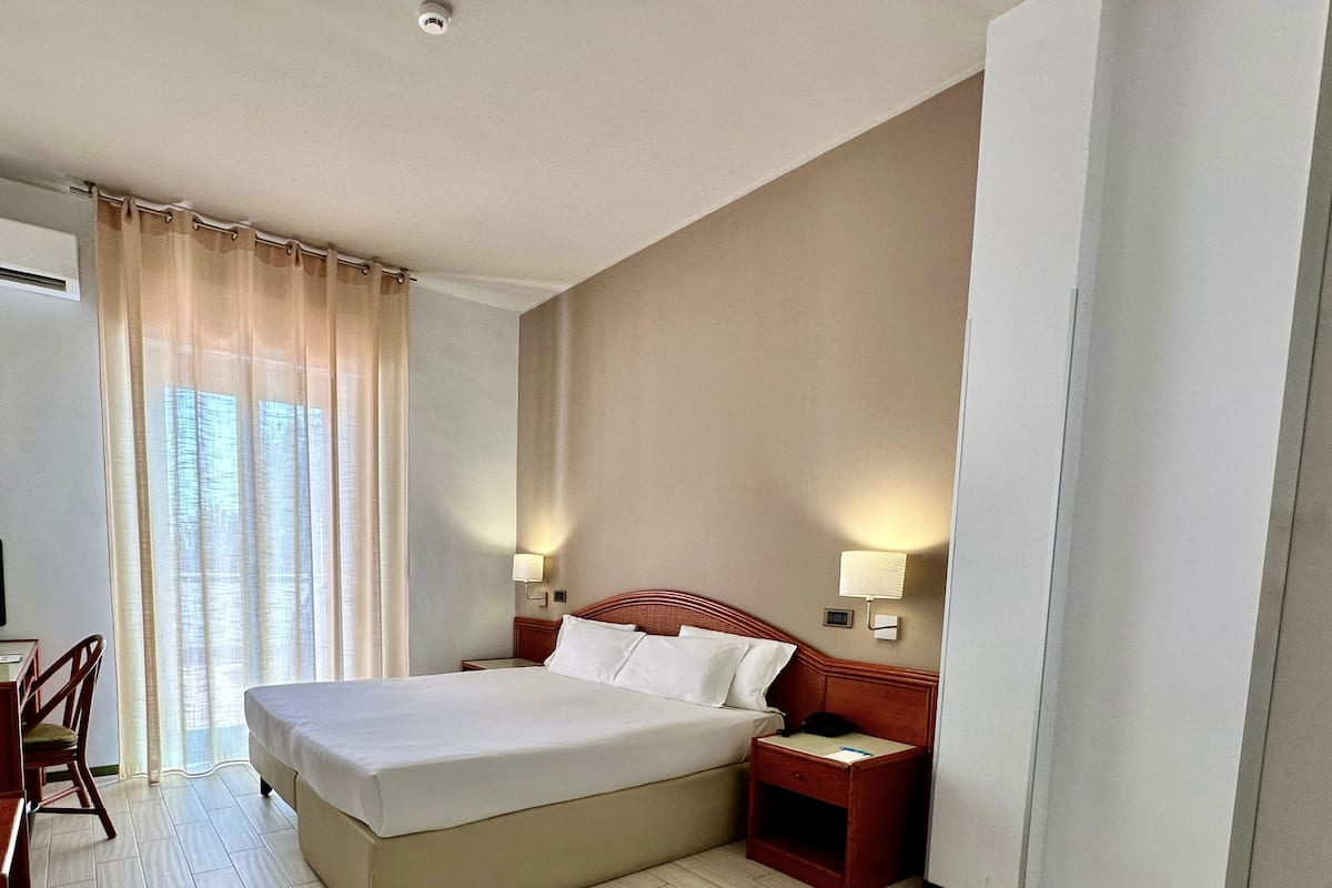 A hotel room with a large bed, two bedside tables, a chair, and a desk.