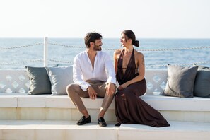A couple sitting on a white outdoor bench with a view of the sea.