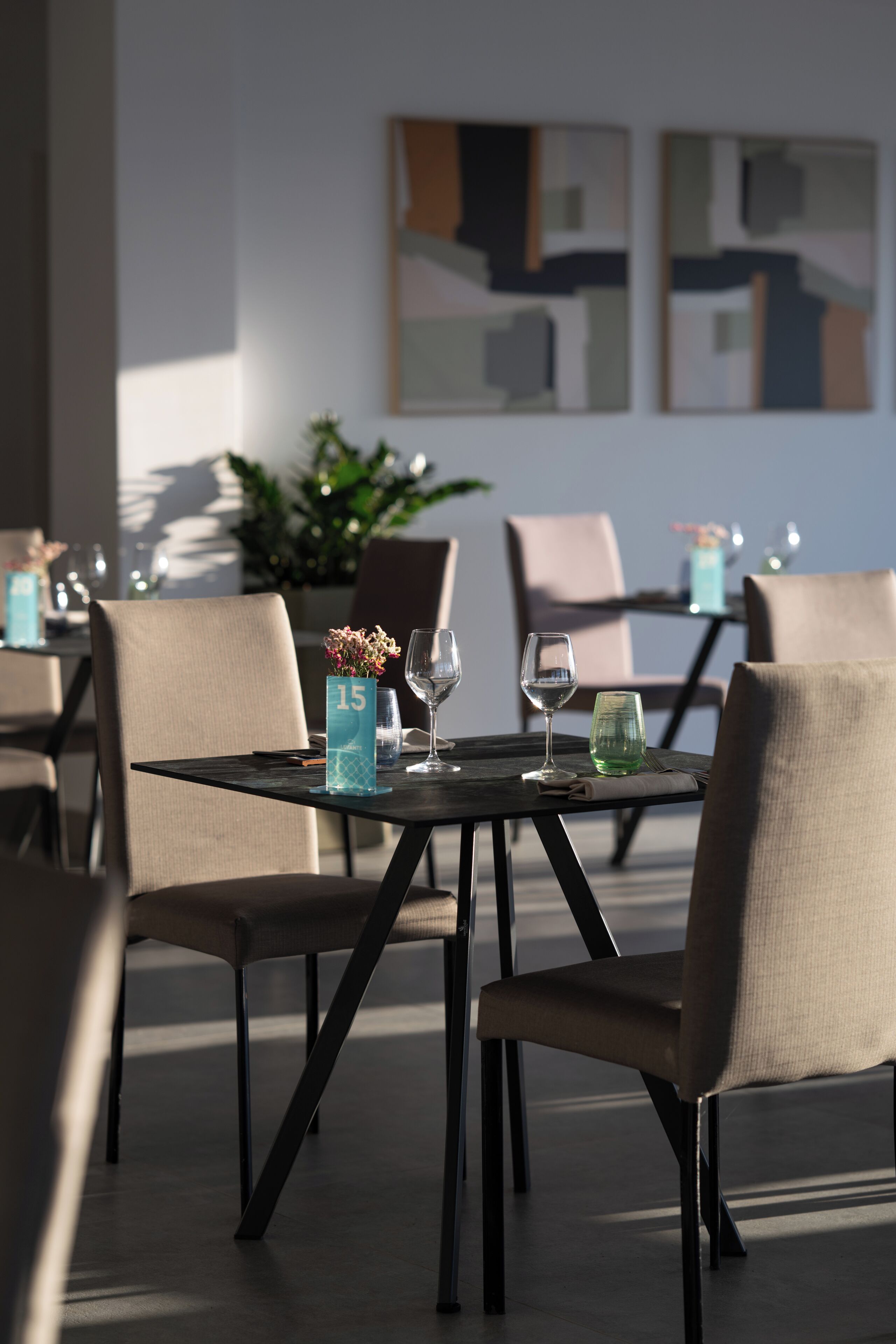 A dining area with tables set for two, each with a numbered placemat, wine glasses, and a small vase with flowers.