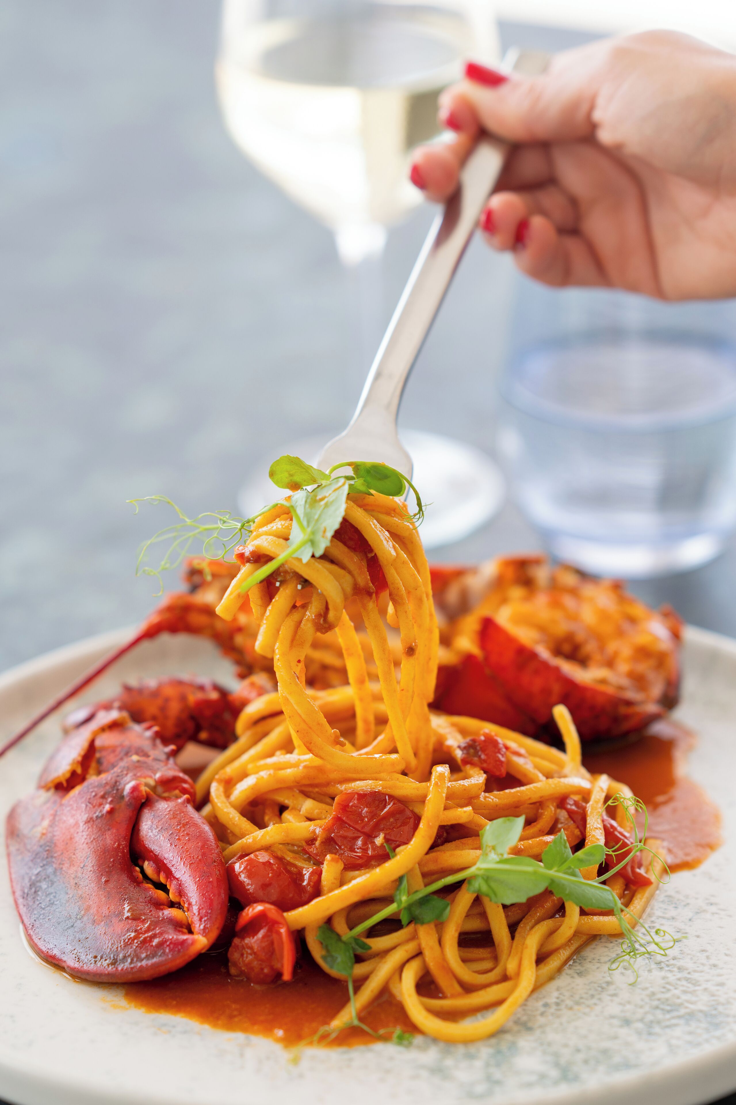 A plate of spaghetti with a lobster tail and greens, held by a fork.