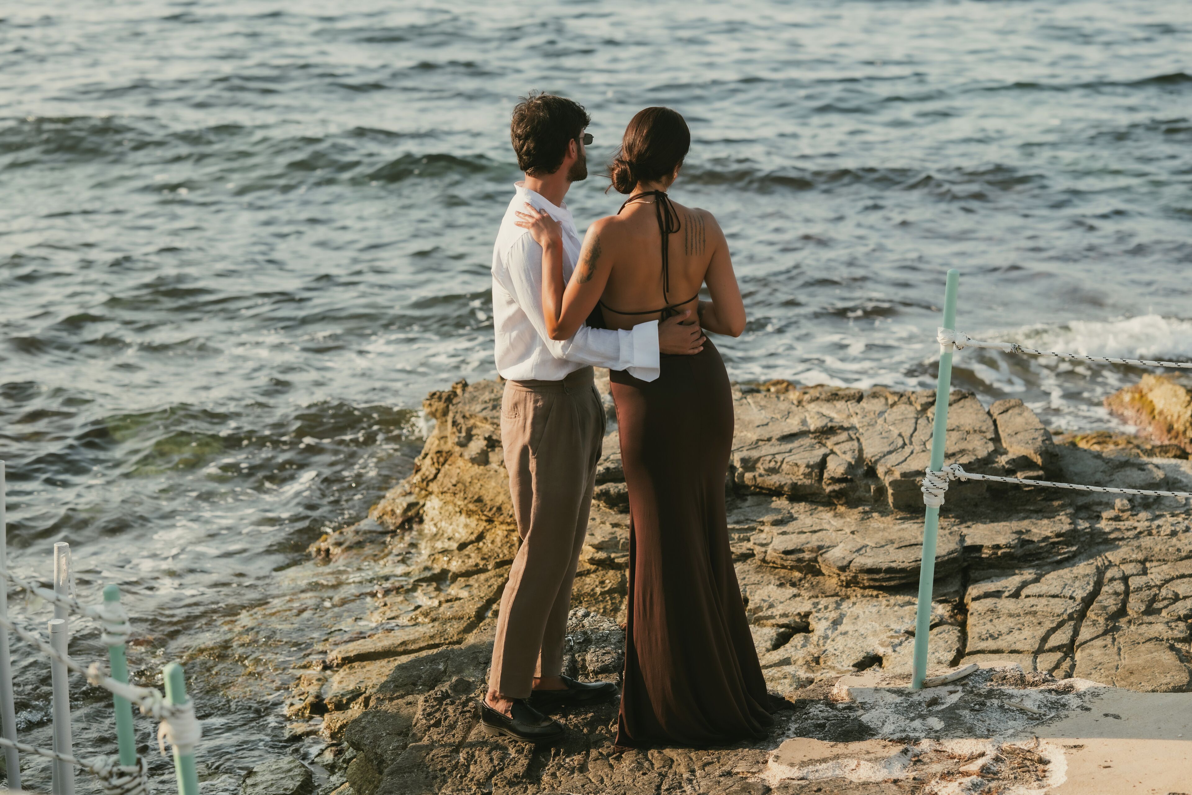 A couple standing on a rocky shore by the sea.