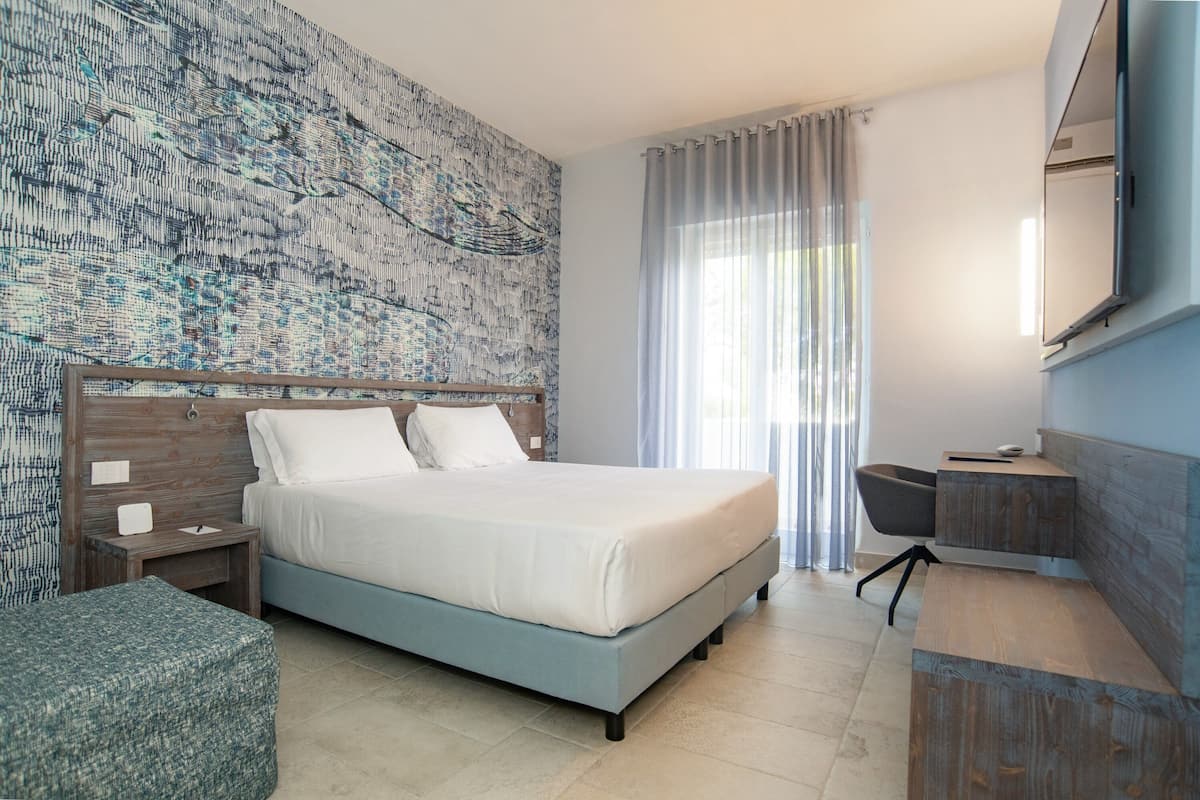 A modern hotel room with a large bed, a wooden headboard, a desk, and a chair.
