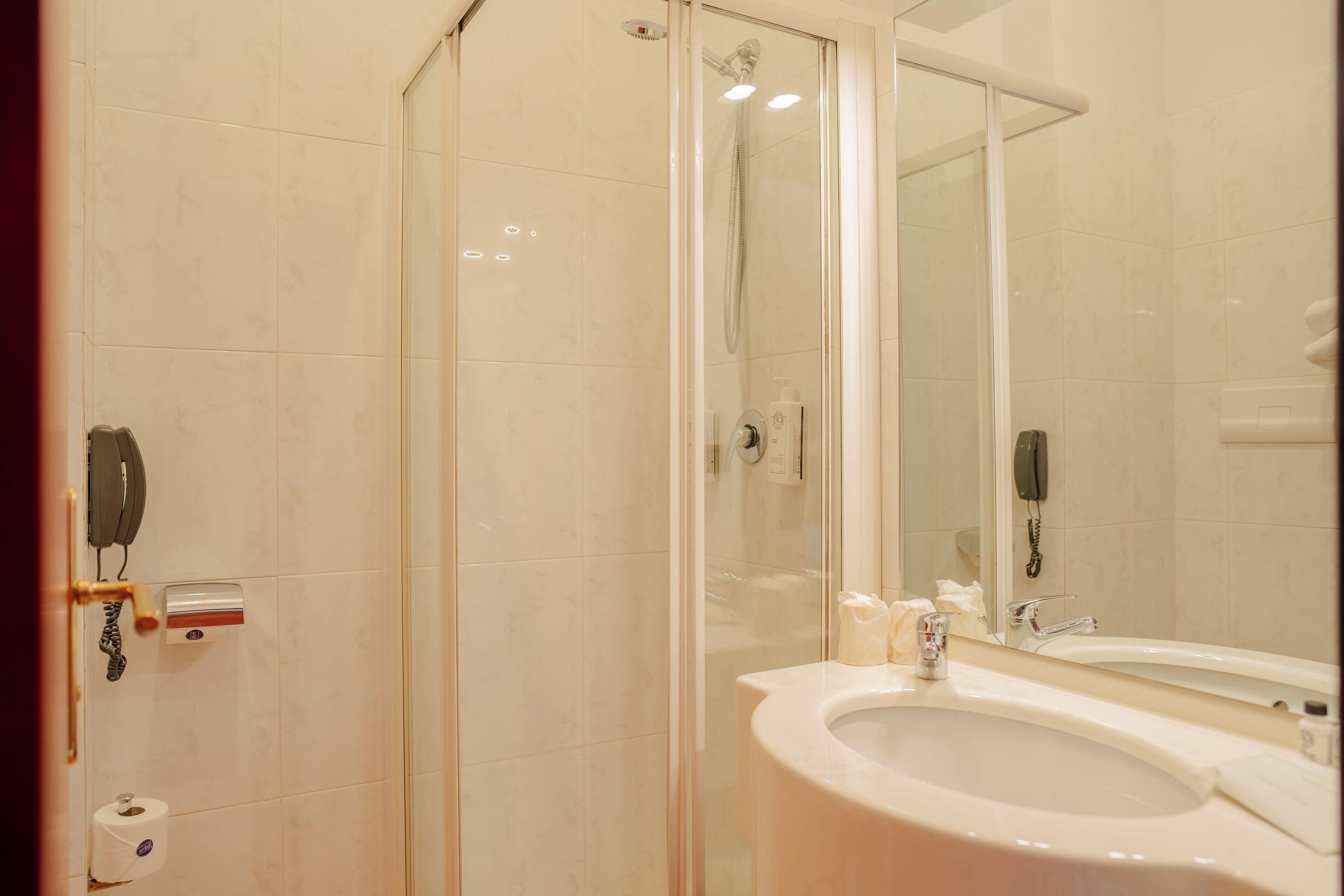 Une salle de bain avec une douche à parois de verre, un lavabo avec un miroir et des toilettes équipées d’un distributeur de serviettes en papier.