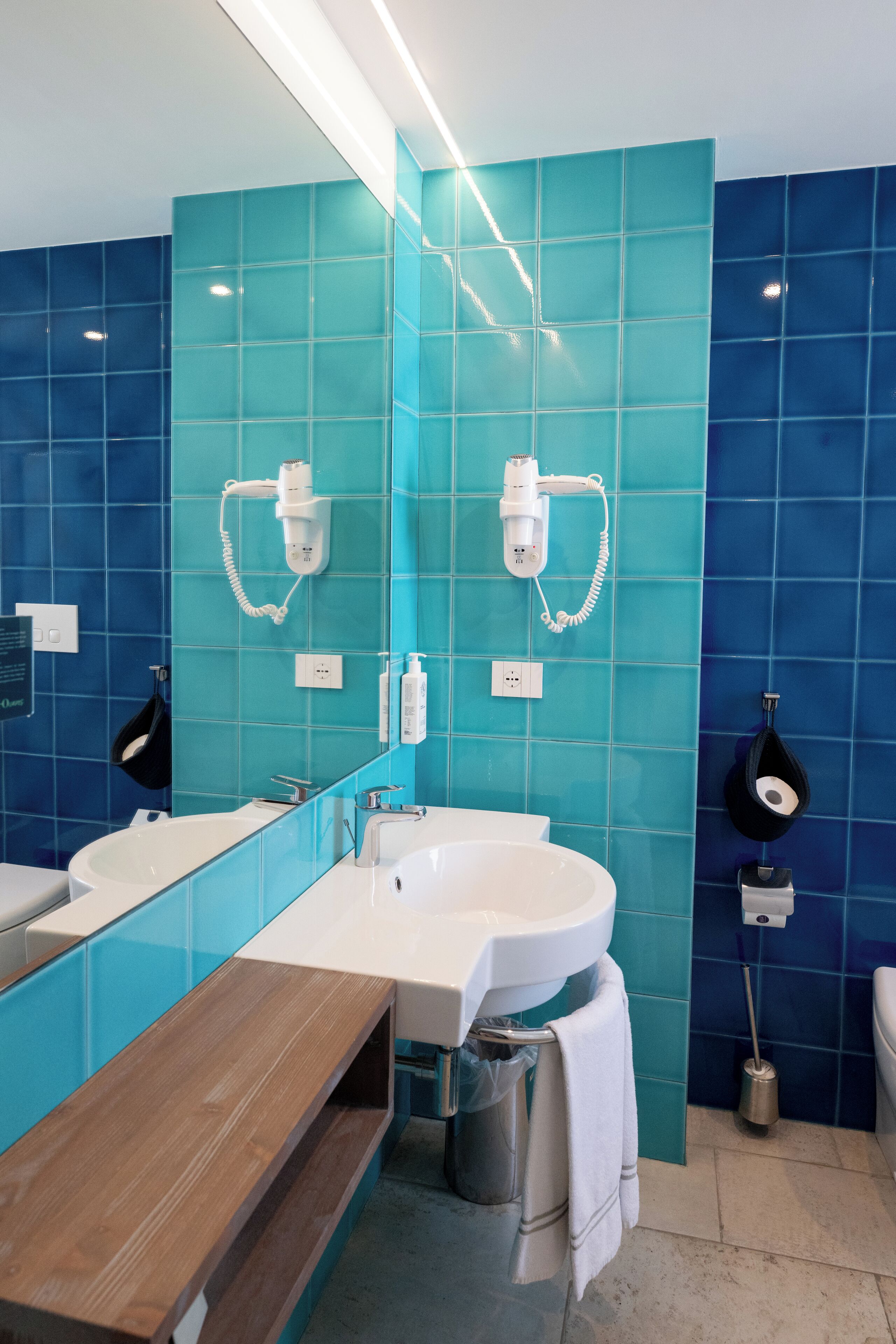 A modern bathroom with a large mirror, two sinks, and a wooden bench.