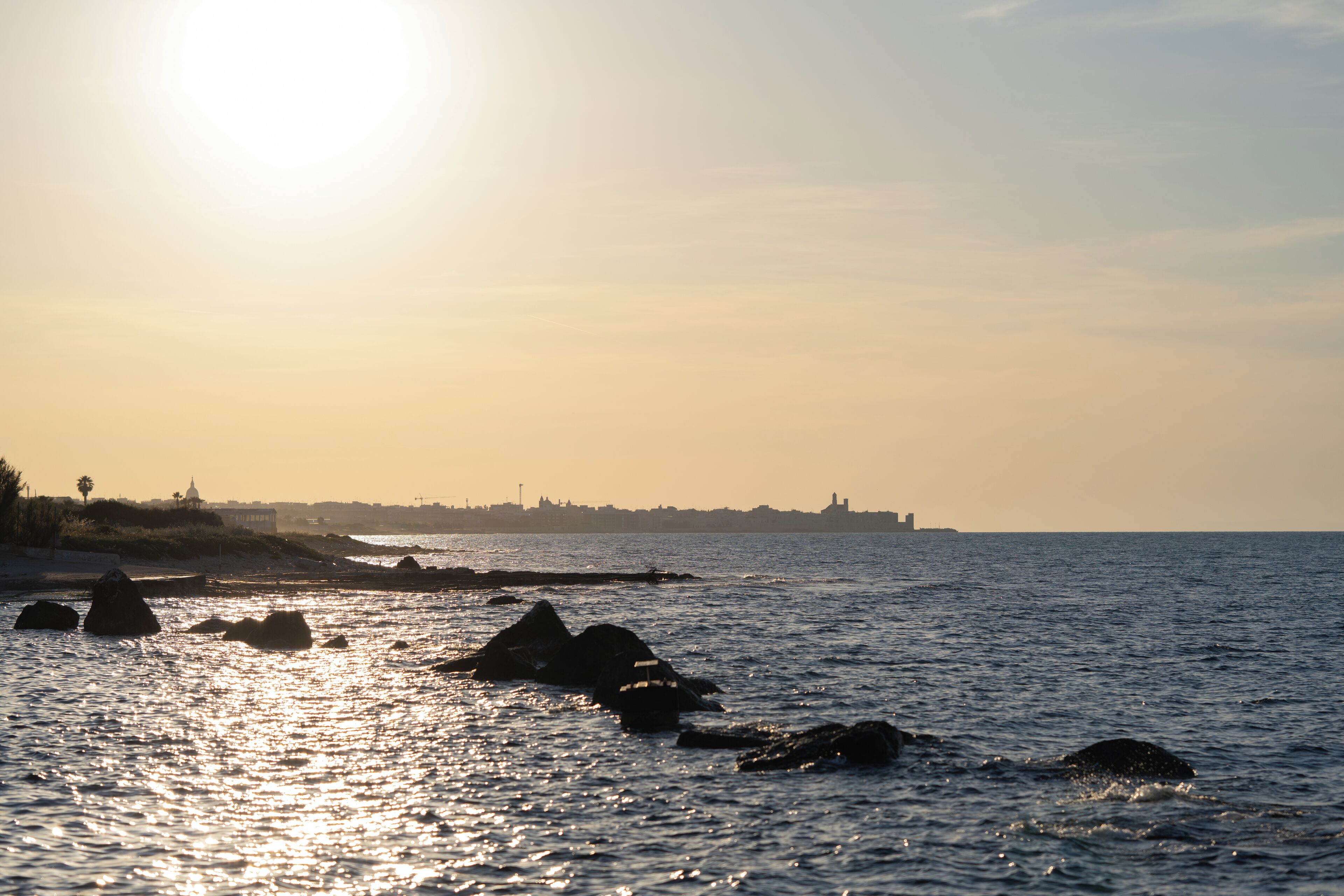 A coastal scene with rocks in the water and a distant shoreline.