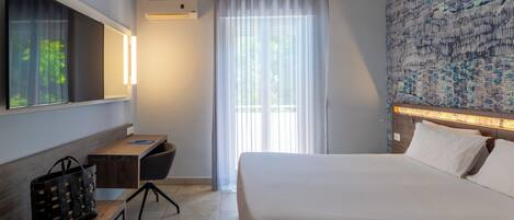 A hotel room with a bed, a desk, a chair, a TV, and a window with curtains.