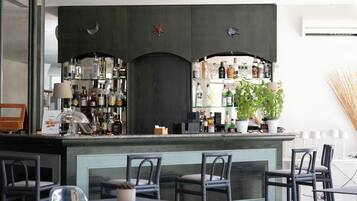 Un área de bar con varias estanterías llenas de botellas de licor, una planta en maceta y taburetes de bar.