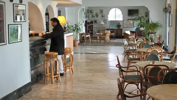 Eine geräumige Lobby mit Barbereich, Korbmöbeln und gerahmten Bildern an den Wänden.