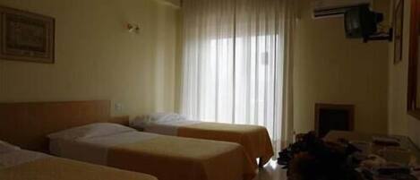 Habitación de hotel con dos camas, una ventana con cortinas, un equipo de aire acondicionado y una mesita con objetos encima.