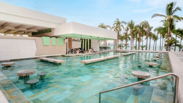 Un espace piscine doté d’un bar, de coins salon et de palmiers.