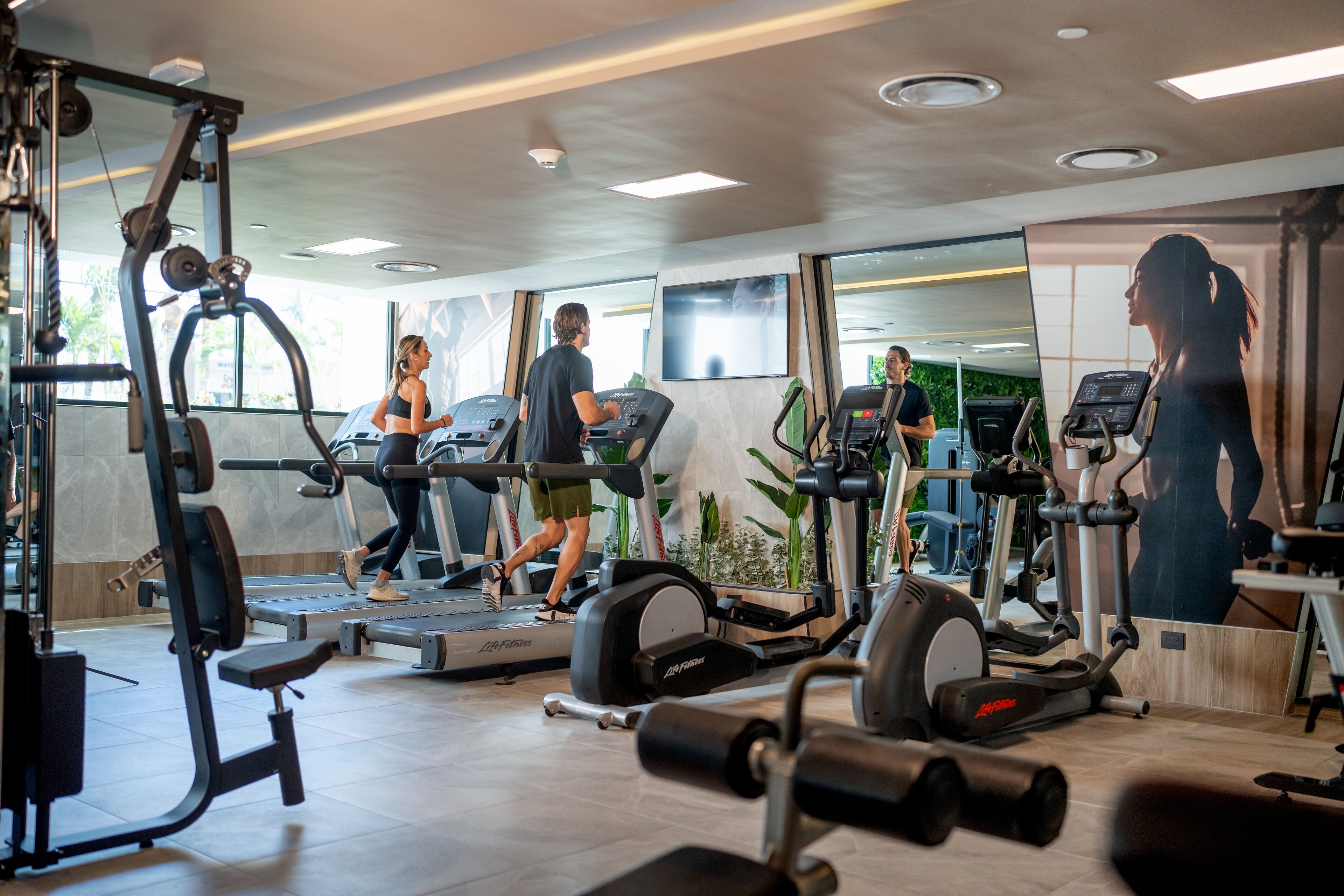 A gym with treadmills, weight machines, and a mirror wall.