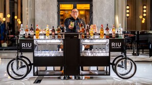Un barman, derrière le comptoir d’un bar appartenant à la chaîne Riu Hotels & Resorts, présente une variété de bouteilles et de verres.