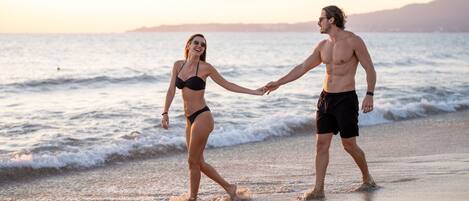 Una pareja tomados de la mano en una playa, con olas al fondo.