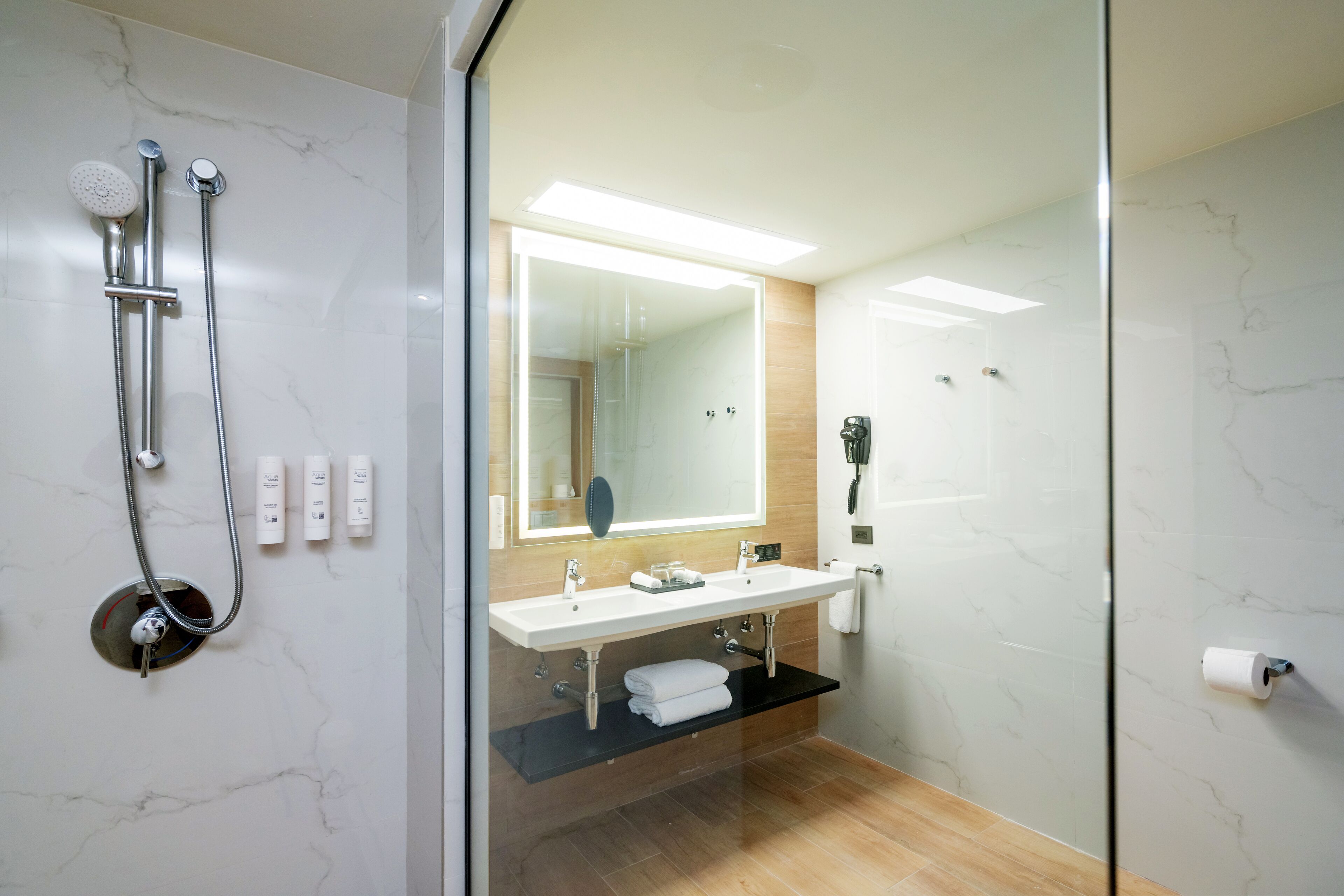 Un baño moderno con cabina de ducha de vidrio, tocador doble y un espejo grande.