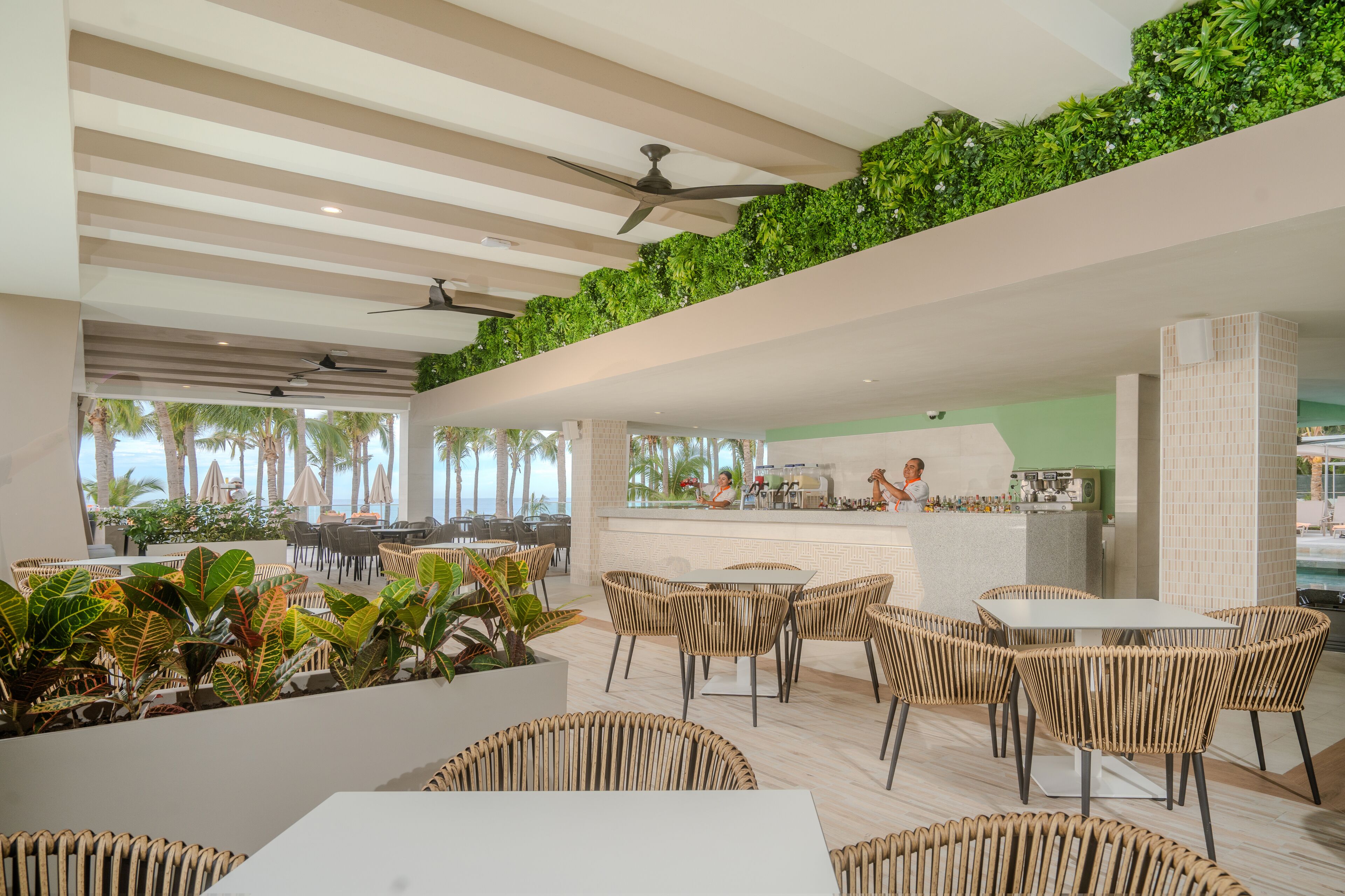 A modern outdoor dining area with wicker furniture, a bar, and a view of palm trees.