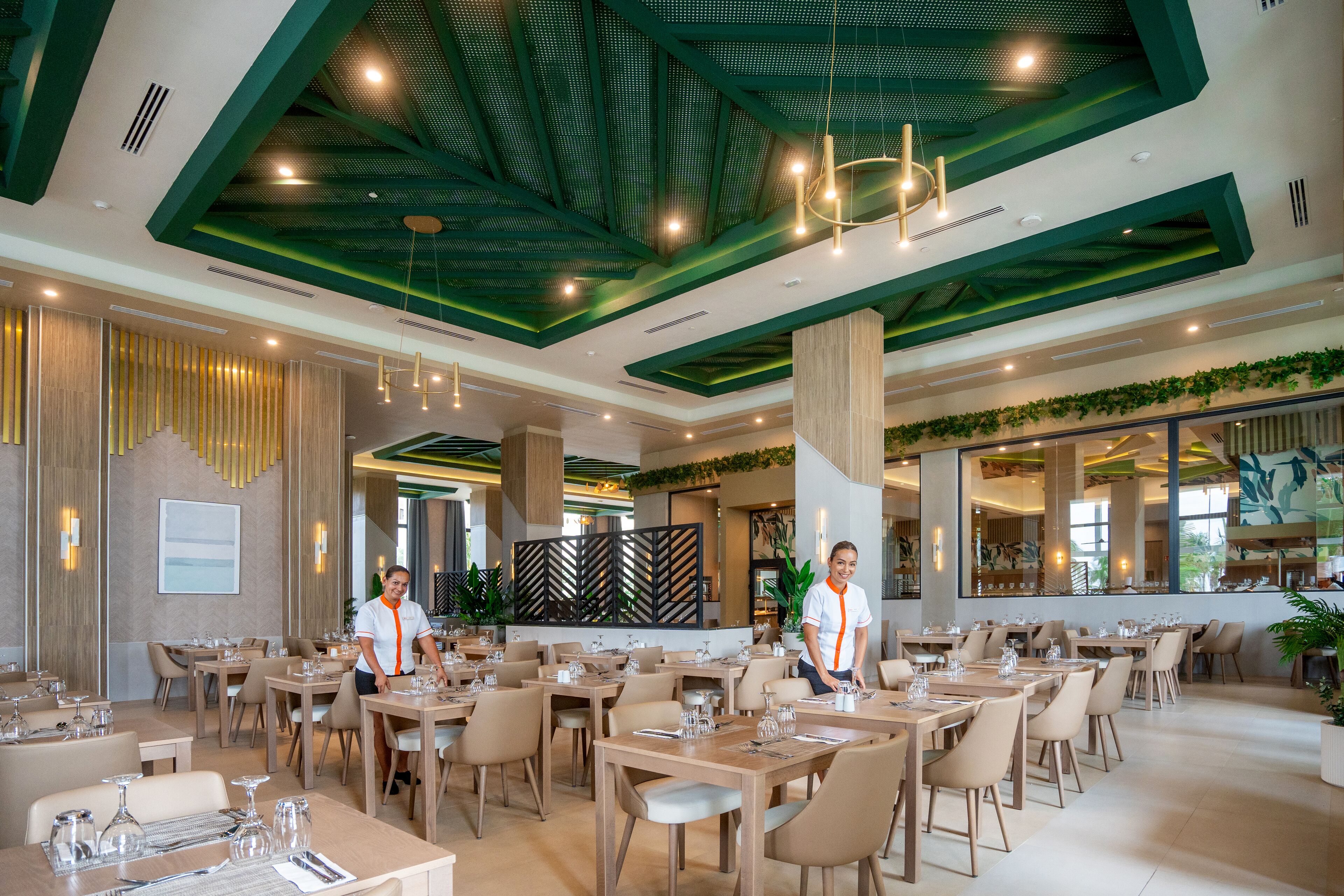 A spacious dining area with multiple tables and chairs, a high ceiling with green accents, and a modern interior design.