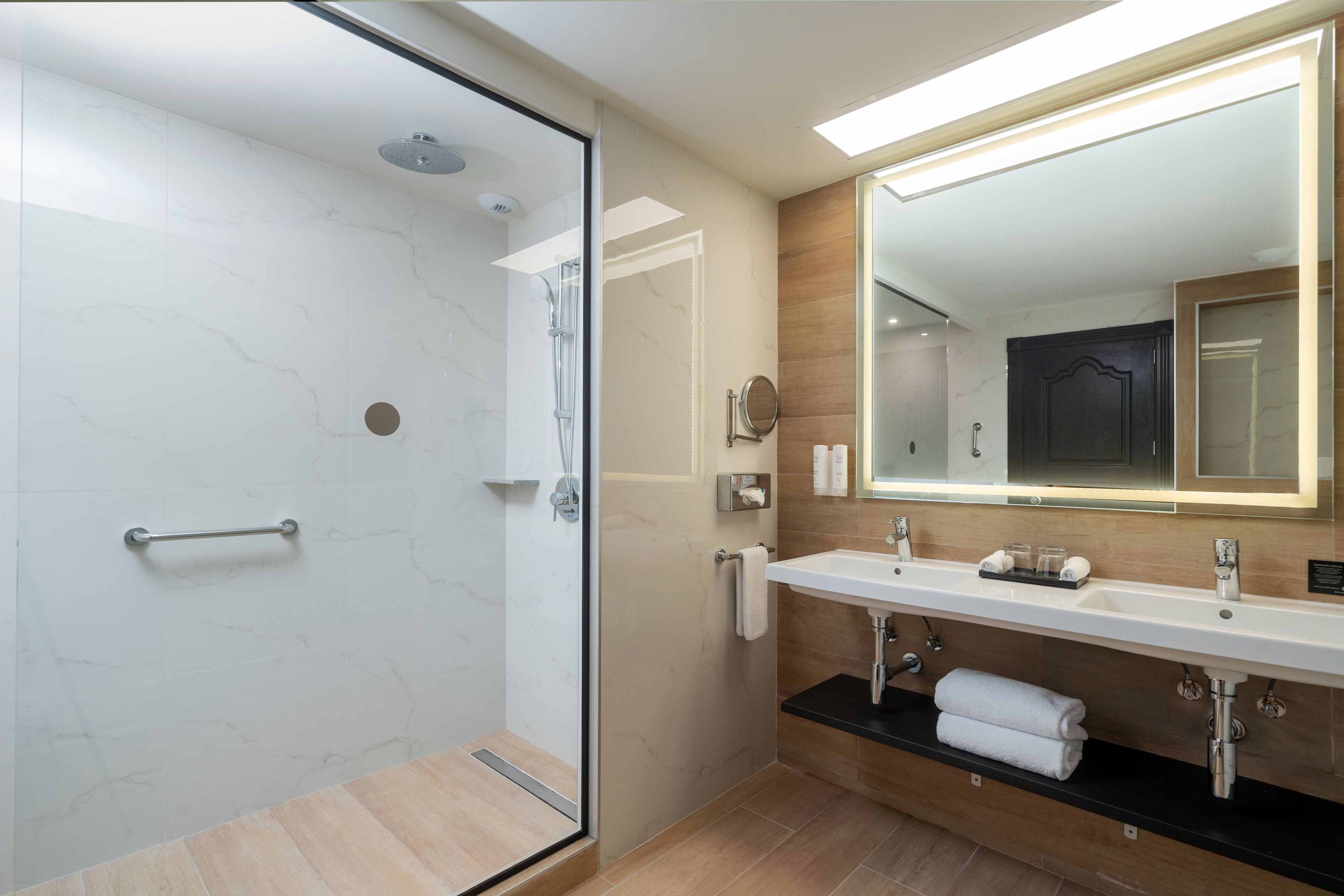Une salle de bain moderne avec une douche à parois de verre, un grand miroir et un meuble-lavabo à deux vasques.