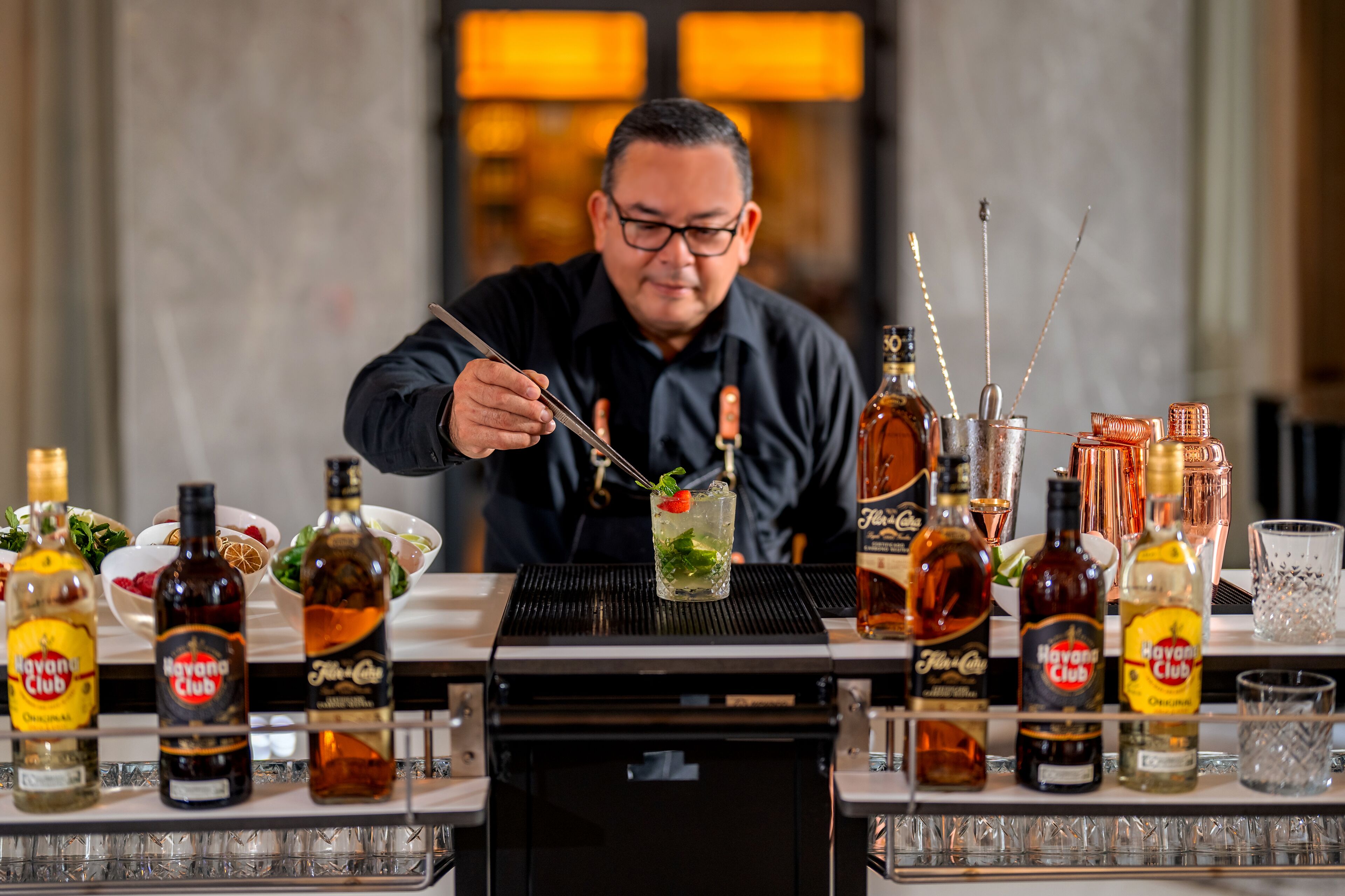 A bartender preparing a drink with various bottles of Havana Club rum and other liquors on a bar counter.
