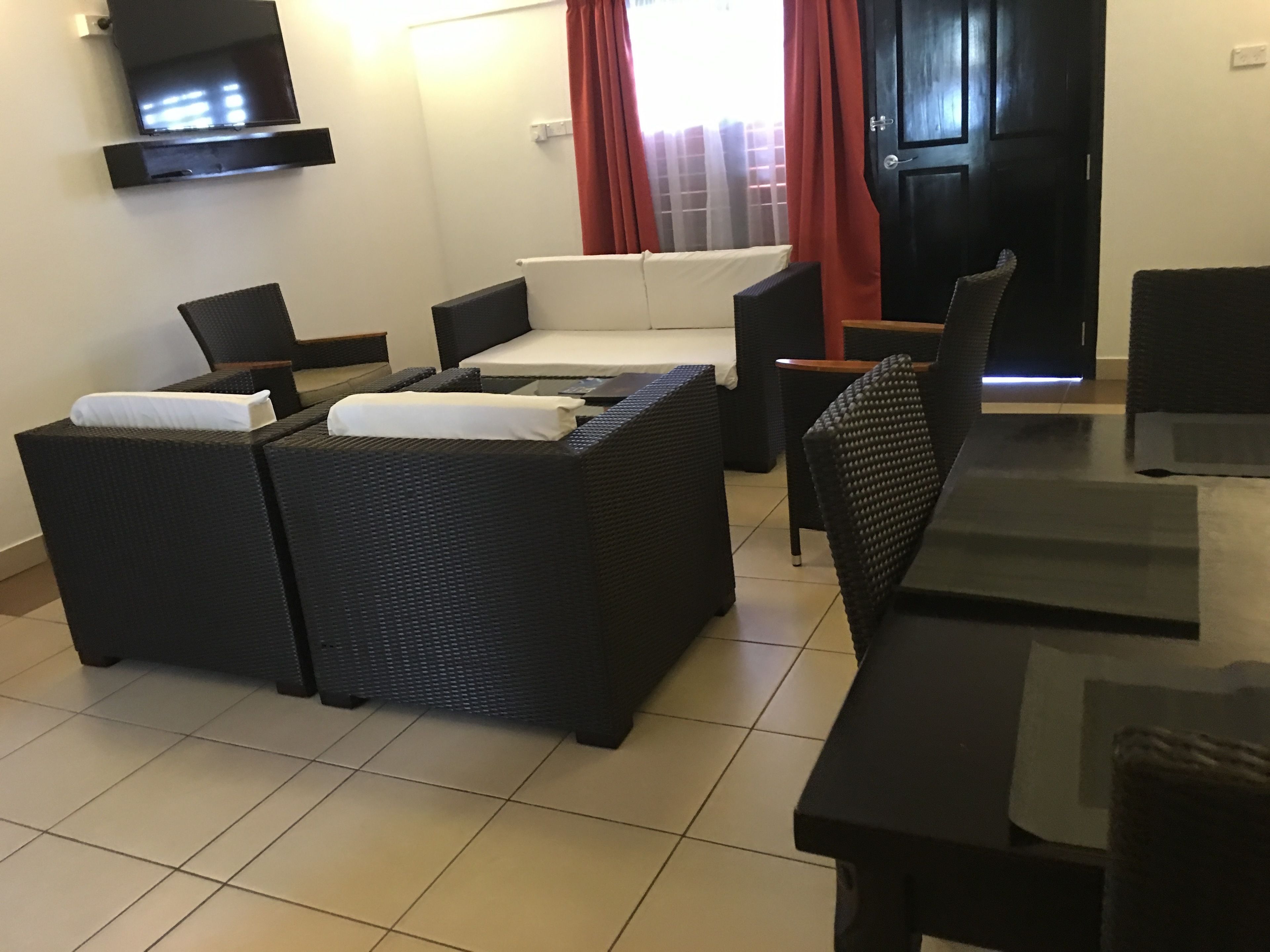 A modern living room with a sofa set, a dining table, and a TV mounted on the wall.