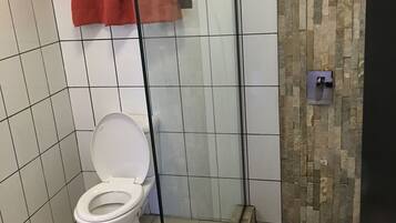 A bathroom with a toilet, a shower area, and a tiled floor.