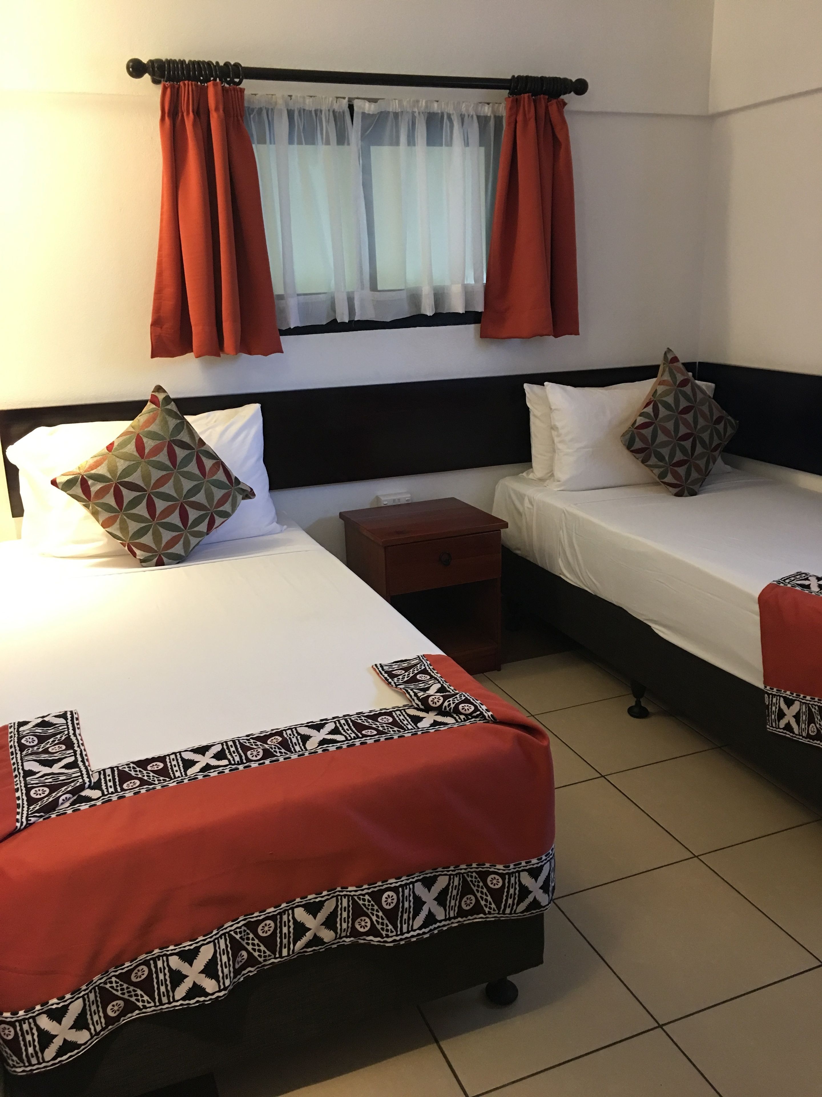 A hotel room with two beds, each with a patterned pillow, a nightstand, and a window with curtains.