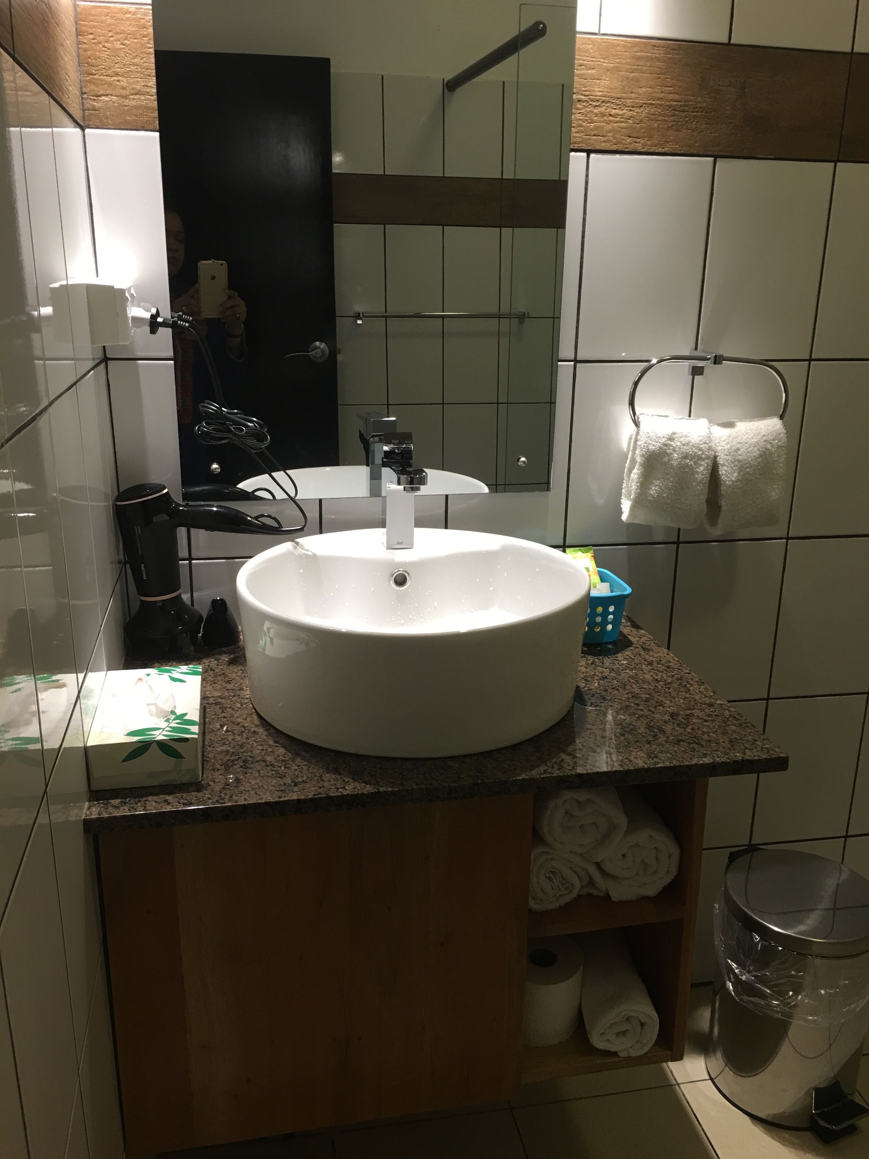 Un baño con lavamanos blanco, espejo, toallero y cubo de basura.