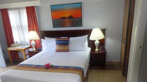A hotel room with a large bed, two bedside tables with lamps, a painting of a sunset, and a view of the sea. - Suva Motor Inn (Suva)