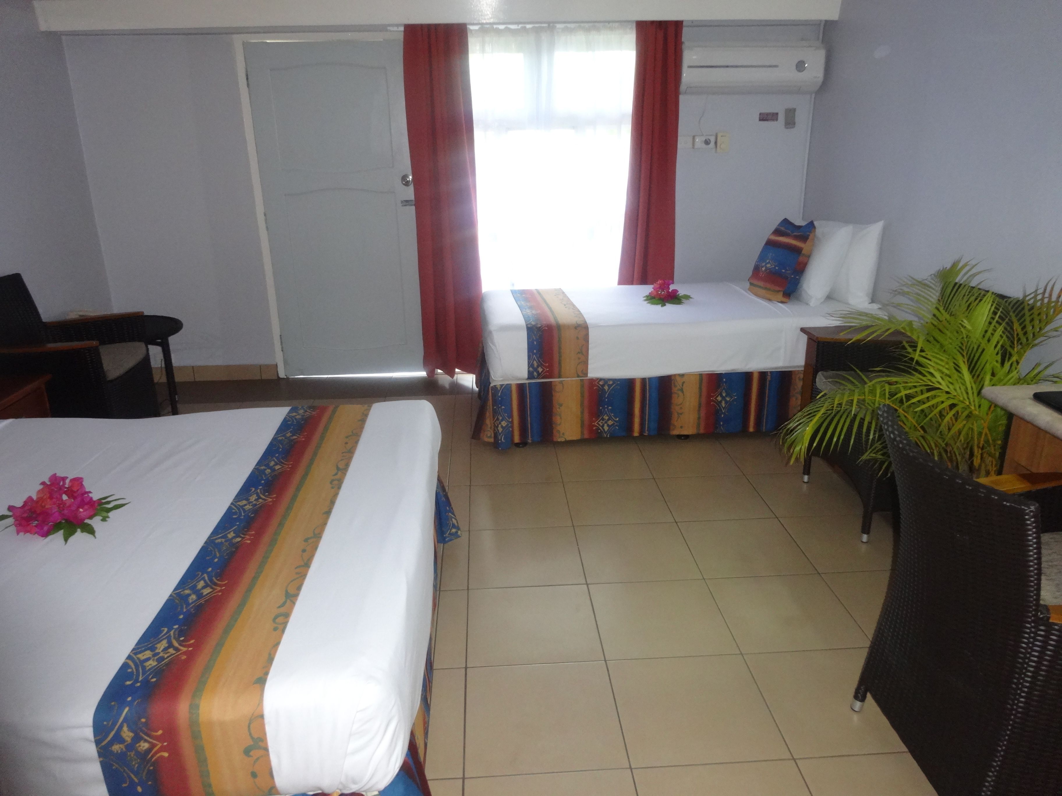 A hotel room with two beds, a chair, a small table, and a potted plant.