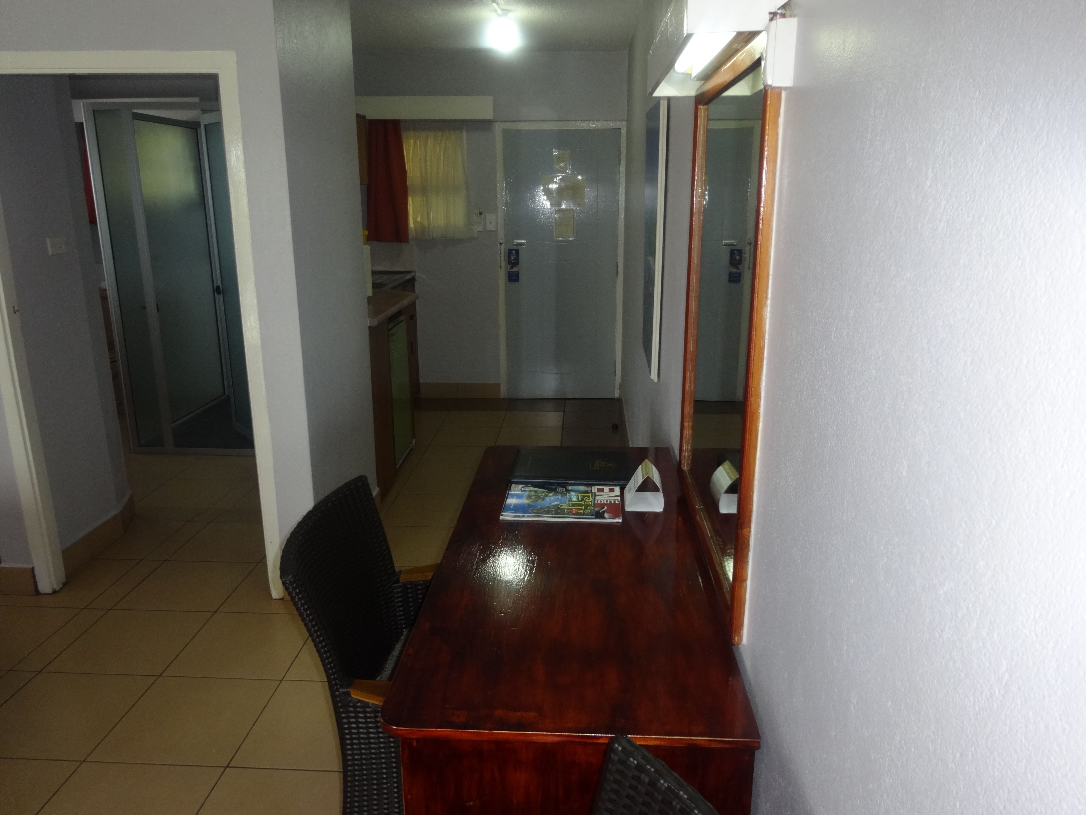 A room with a wooden dining table, two chairs, a small kitchen area, and a door leading to another room.